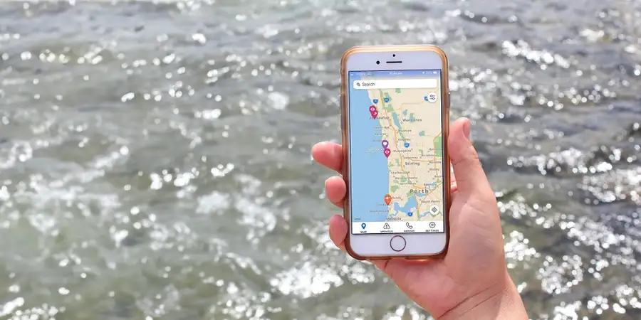 Hand holding a smartphone displaying a map app, with a flowing river in the background.