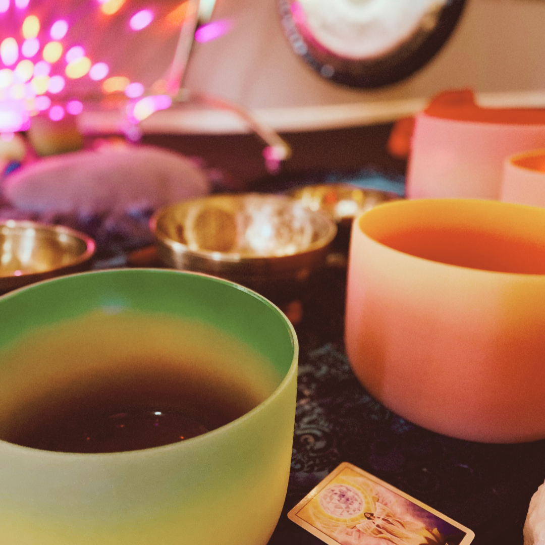 An assortment of crystal and Tibetan singing bowls with gongs in the background.