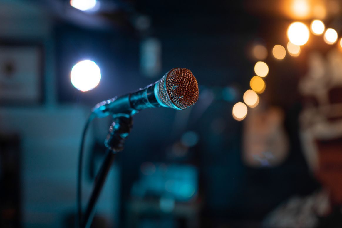 Close-up of a microphone on a stand with blurred stage lights in the background, creating a moody performance atmosphere.