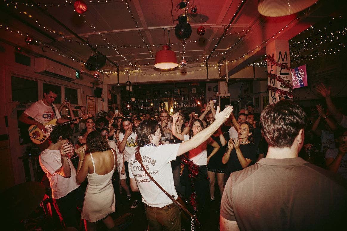 People dancing and enjoying live music in a dimly lit venue with string lights and a lively atmosphere.