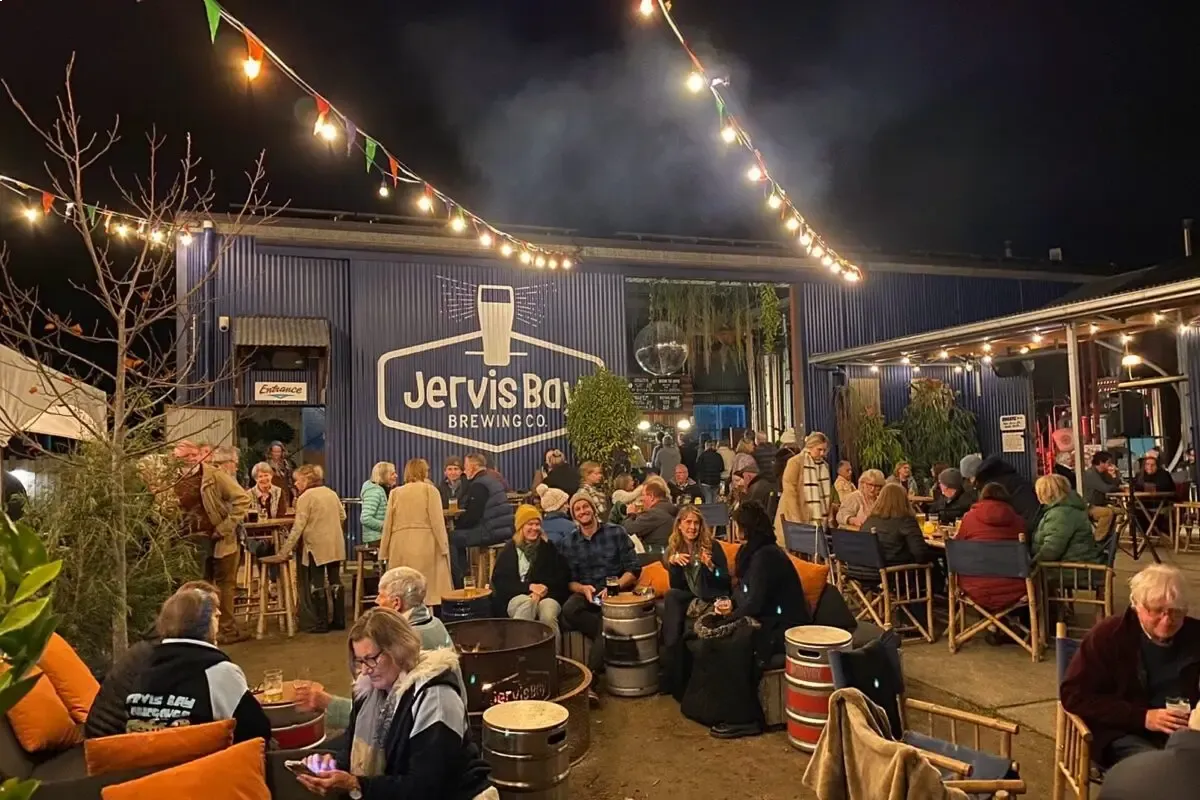 Outdoor evening gathering at Jervis Bay Brewing Co. with people sitting, talking, and enjoying drinks under string lights.