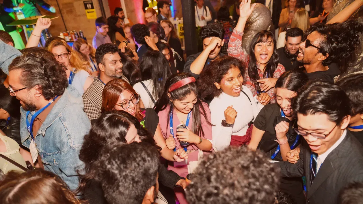 A joyful crowd of people smiling and dancing at a lively indoor party, with colorful lights and lively atmosphere.