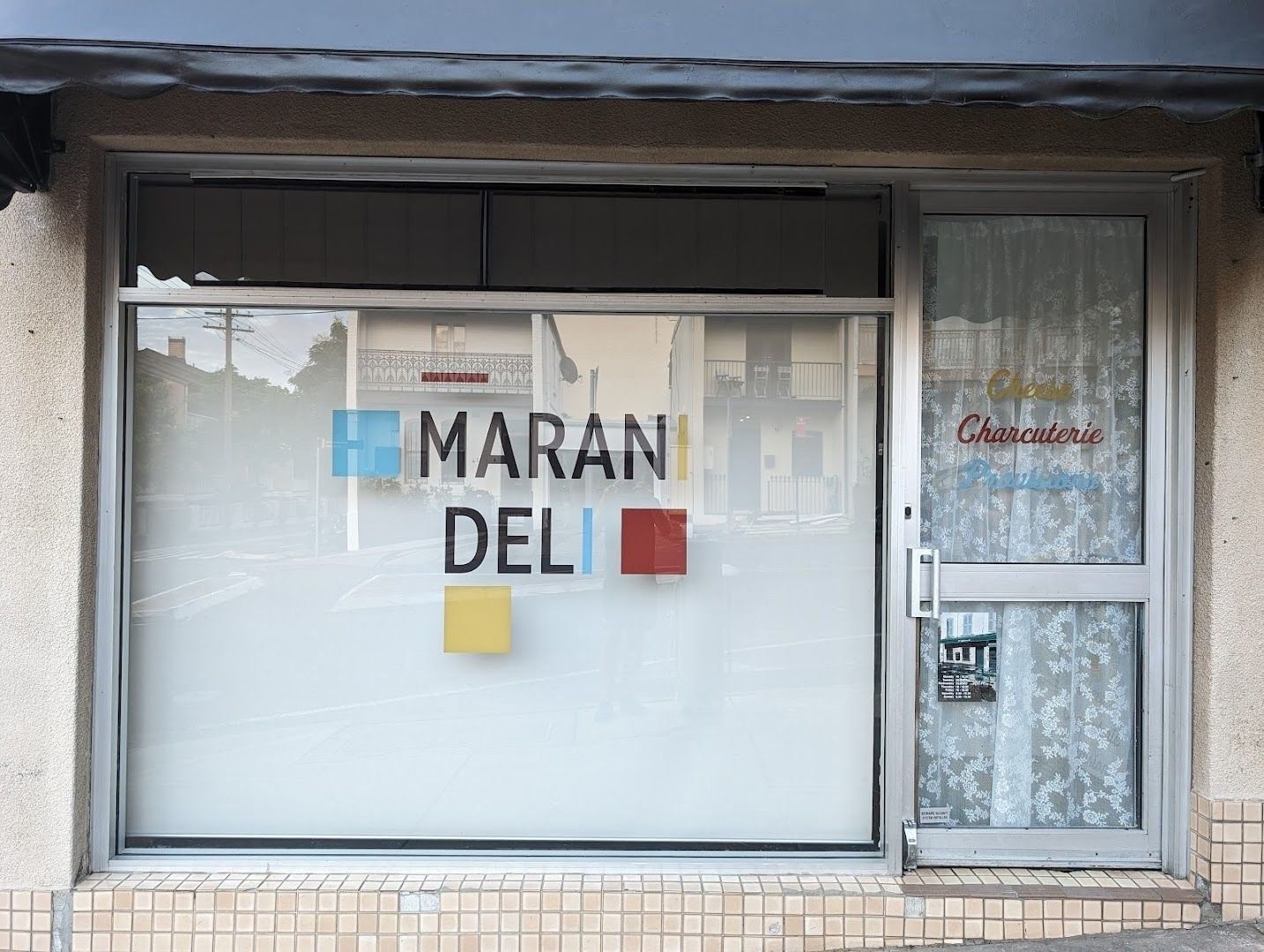 Storefront with sign reading "Marani Deli" on frosted glass; adjacent door has "Chez Charcuterie" written on it.