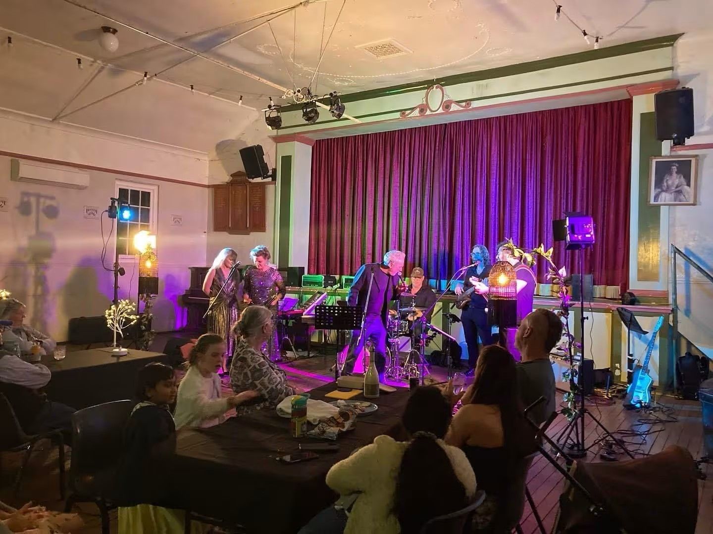 Live music being performed by a six piece band with dim lighting and an audience
