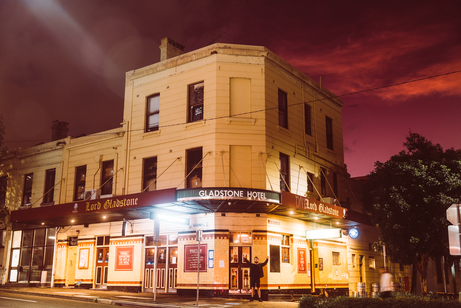 Historic hotel building with illuminated facade and signs, against a dramatic purple and pink evening sky.