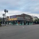 Corner view of a two-story brick building with large windows, situated on an empty intersection with traffic lights under a cloudy sky.