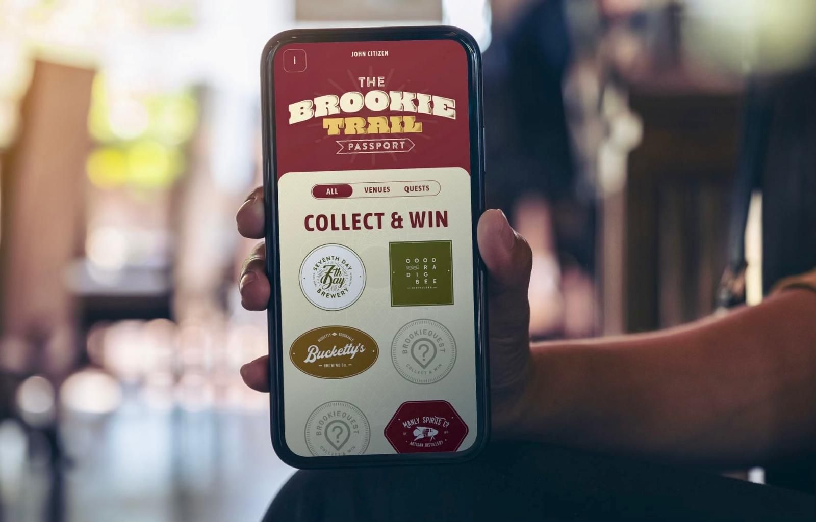 A hand holds an iPhone on the screen we see the Hoppy Trails Passport
