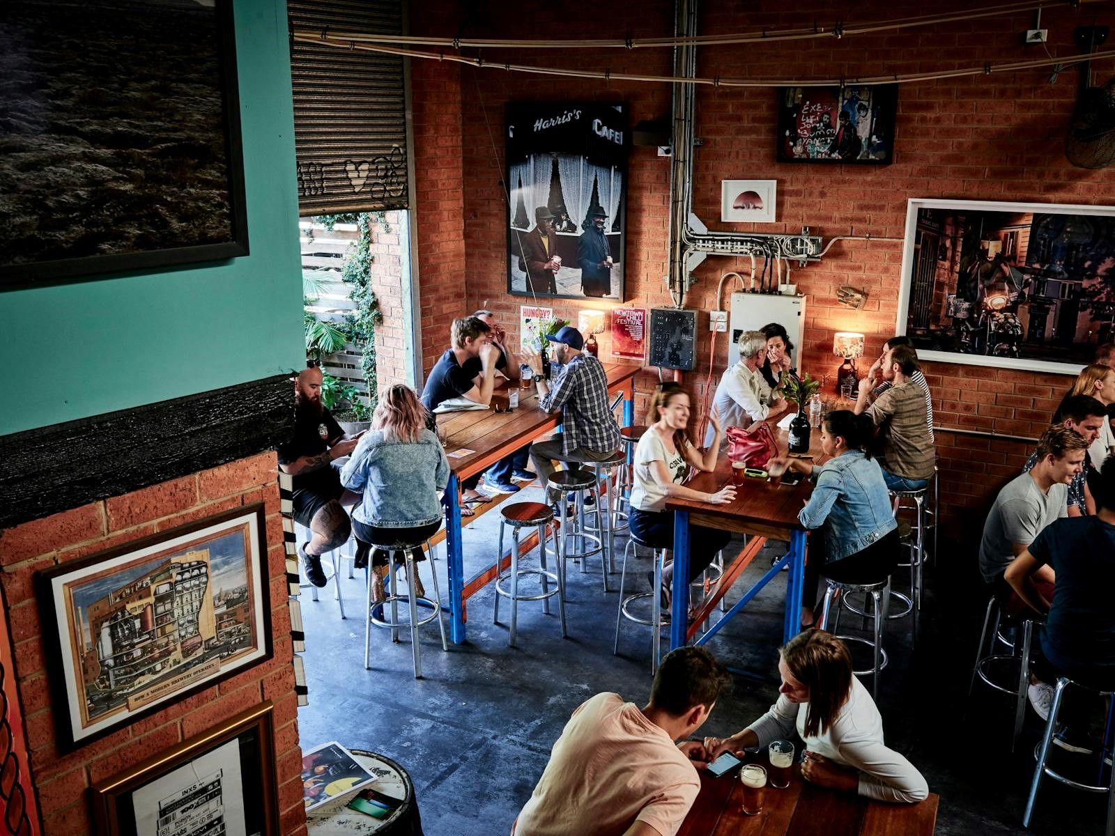 A lively cafe scene with people seated at high tables, chatting and enjoying drinks, surrounded by eclectic wall art and warm lighting.