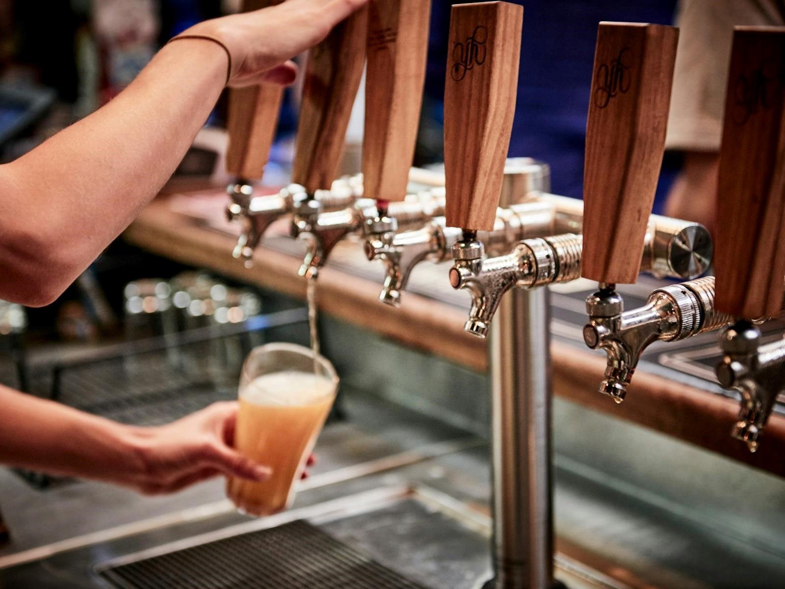 A person pours beer from a row of wooden-handled taps into a glass at a bar.