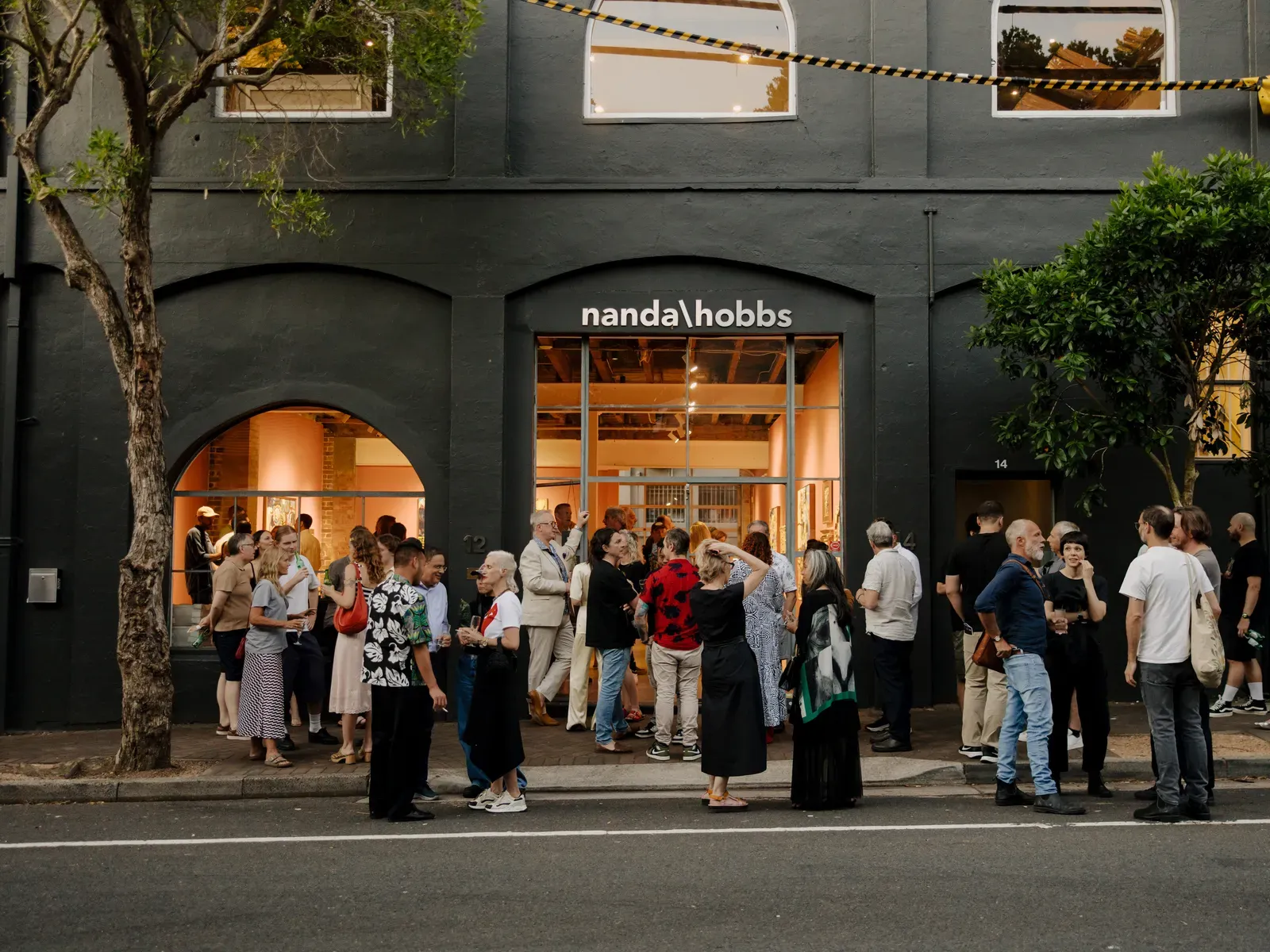 People gather outside the entrance of Nanda\Hobbs gallery under evening lights, engaging in conversation on a city street.