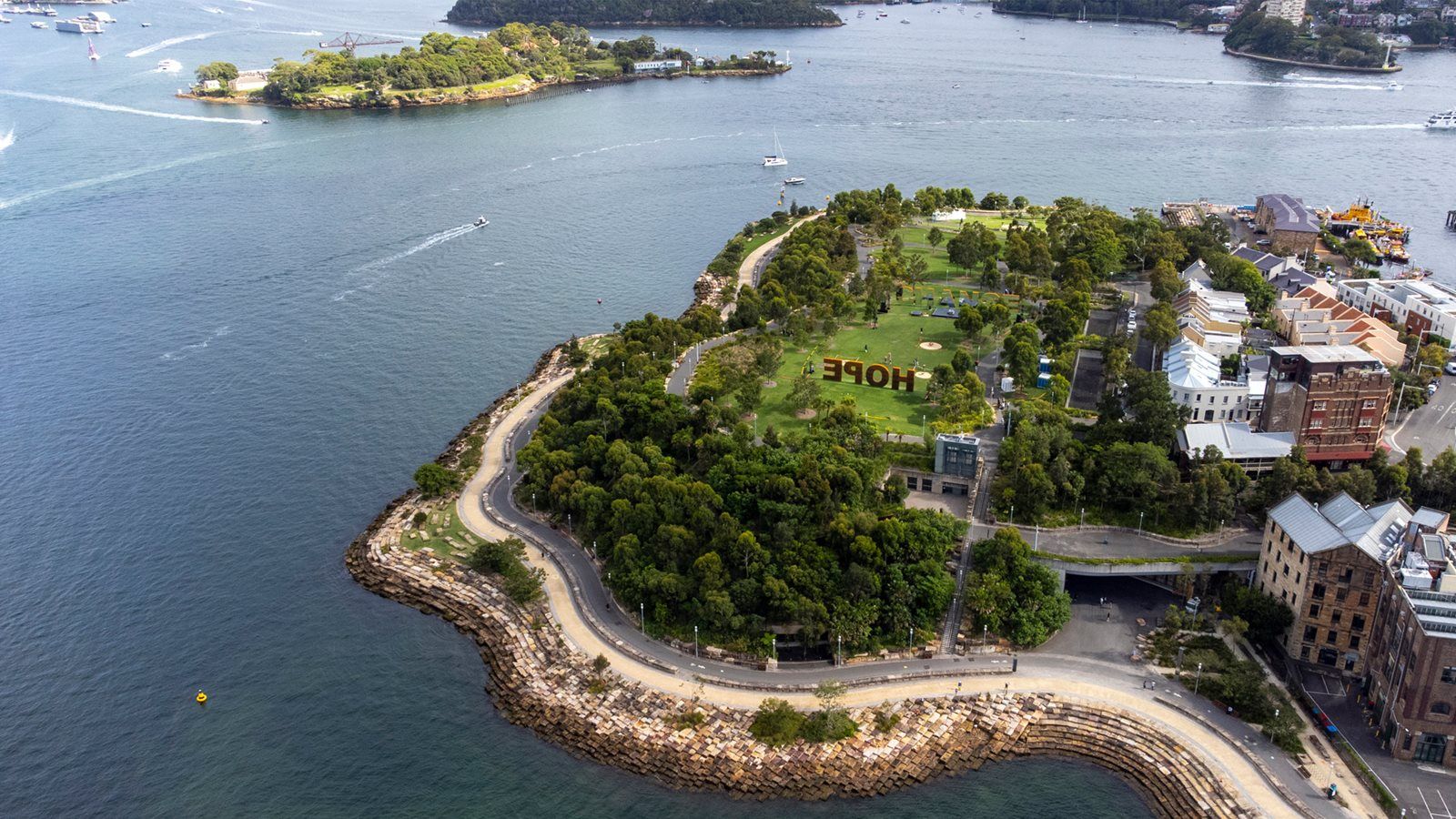 Aerial view of an island with lush greenery and the word "HOPE" spelled out in large letters on the grass, surrounded by water and buildings.