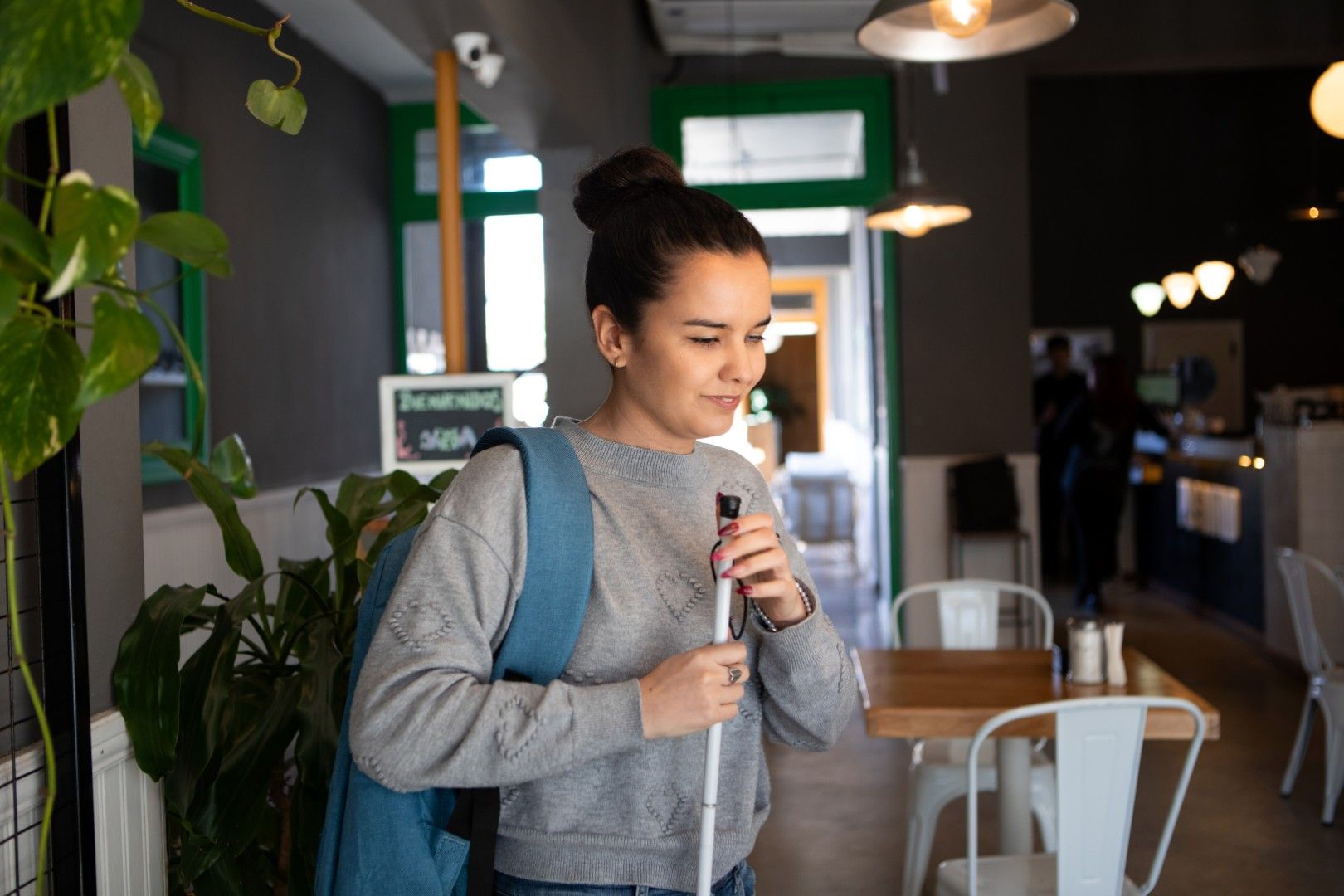Young vision impaired lady walks through a cafe carrying a white cane