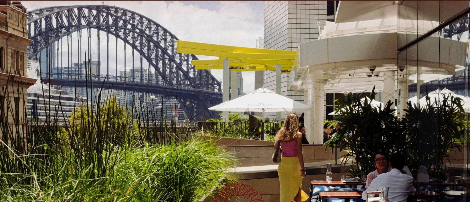 Rooftop dining area with plants and umbrellas overlooking the Sydney Harbour Bridge. A woman in a pink top and yellow skirt walks by.