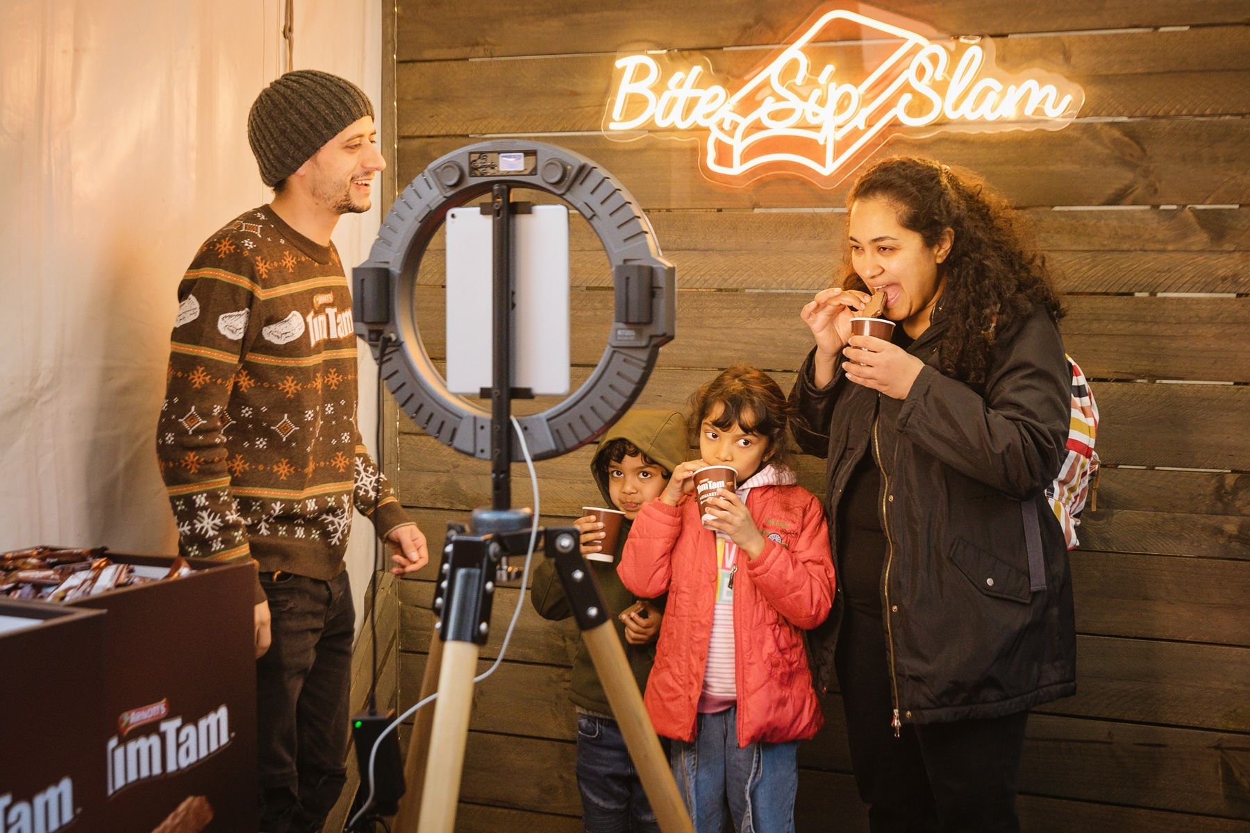 A family standing in front of a selfie ring light, eating Tim Tams