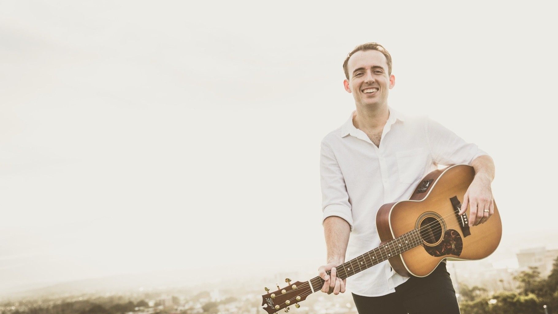 Tim holding a guitar and smiling at the camera.