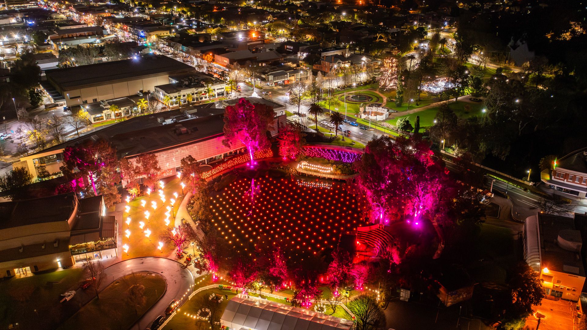 A lake filled with illuminated floating lights and surrounded by artworks at night