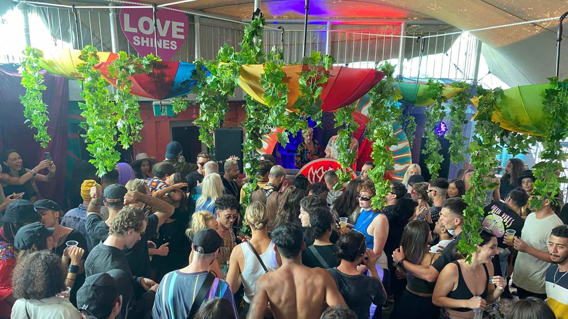 Crowd enjoying a lively party under colorful decorations and greenery, with a "Love Shines" banner in the background.