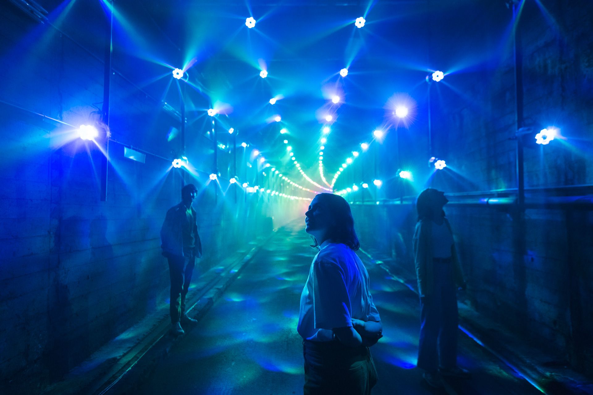 People walking through a railway tunnel, surrounded by archways of lighting effects
