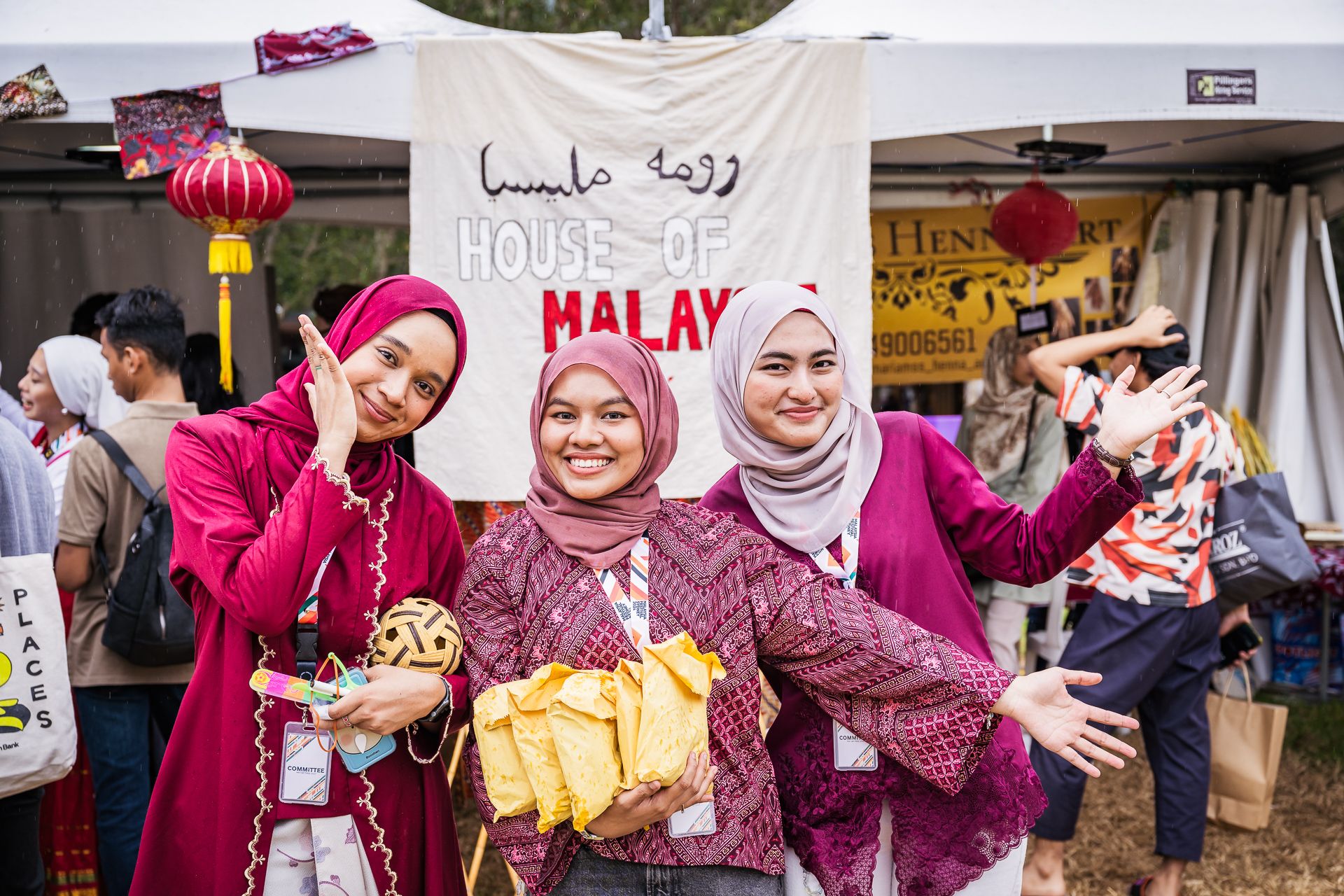 Three women wearing vibrant traditional Malaysian outfits smiling at the camera during the Malaysian Festival in Darling Harbour.
