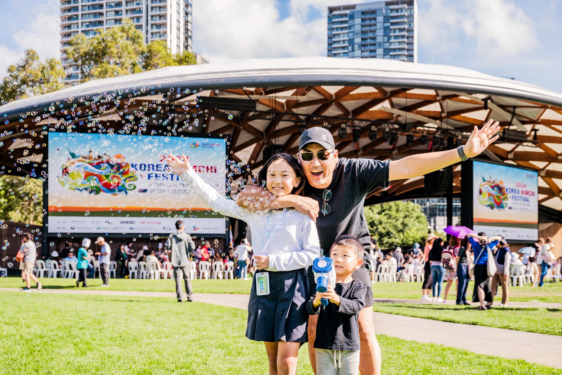 A candid moment of a family with a young child chasing bubbles in front of the festival stage at the Korean Festival in Darling Harbour.