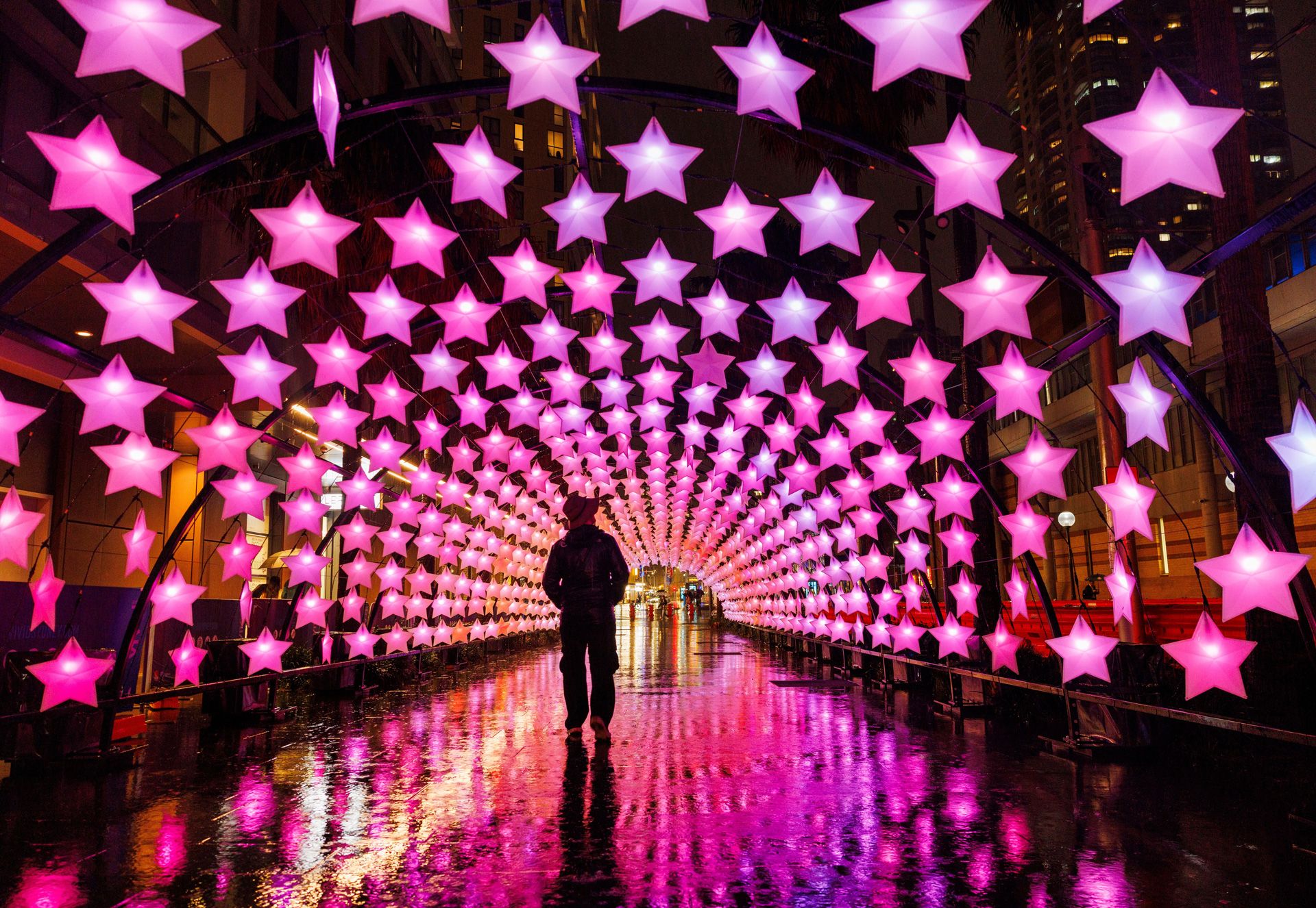 A person wanders through a long tunnel of illuminated hanging stars