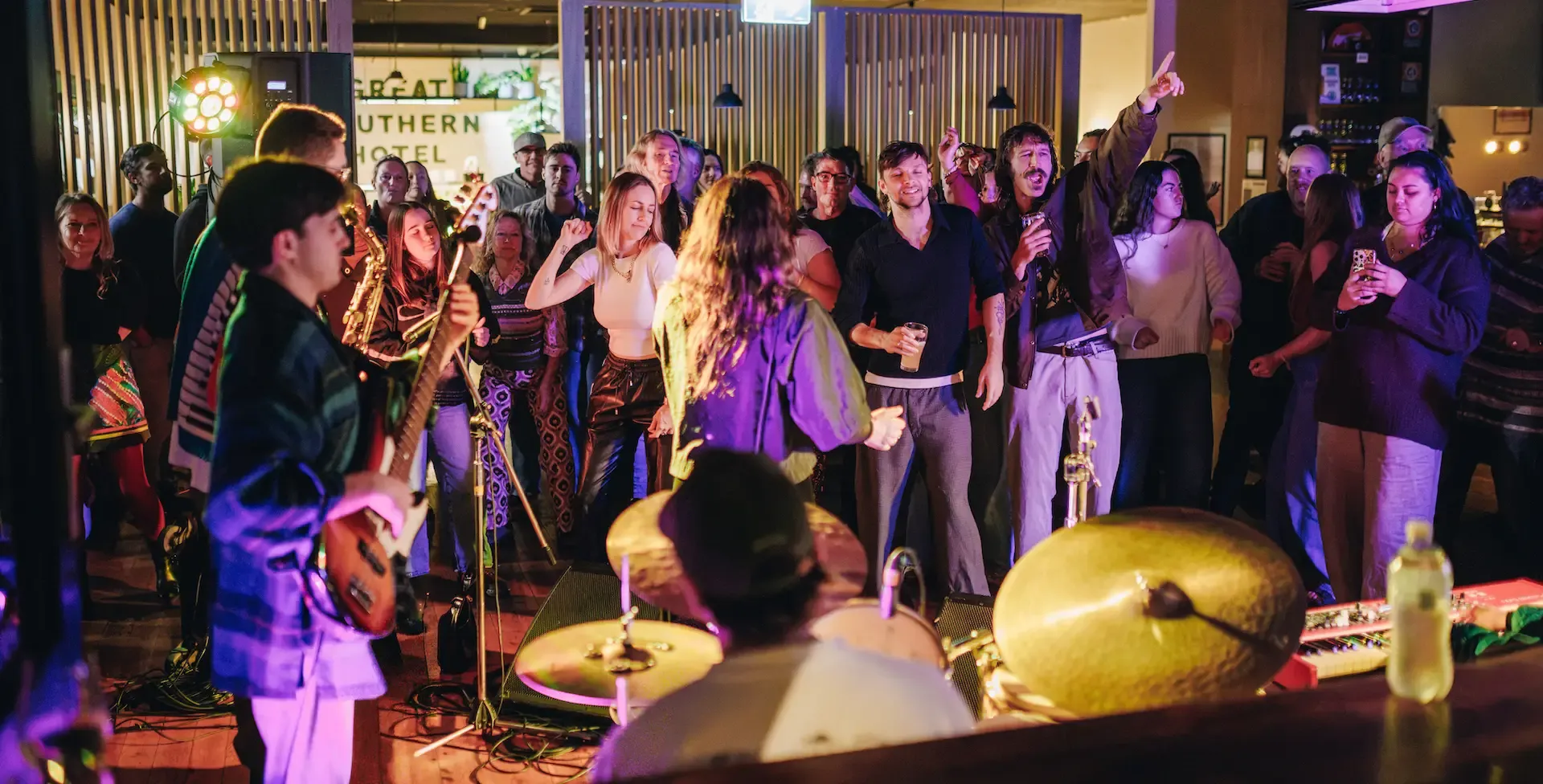 A lively band performs on stage as a diverse crowd dances and enjoys the music in a warmly lit venue.