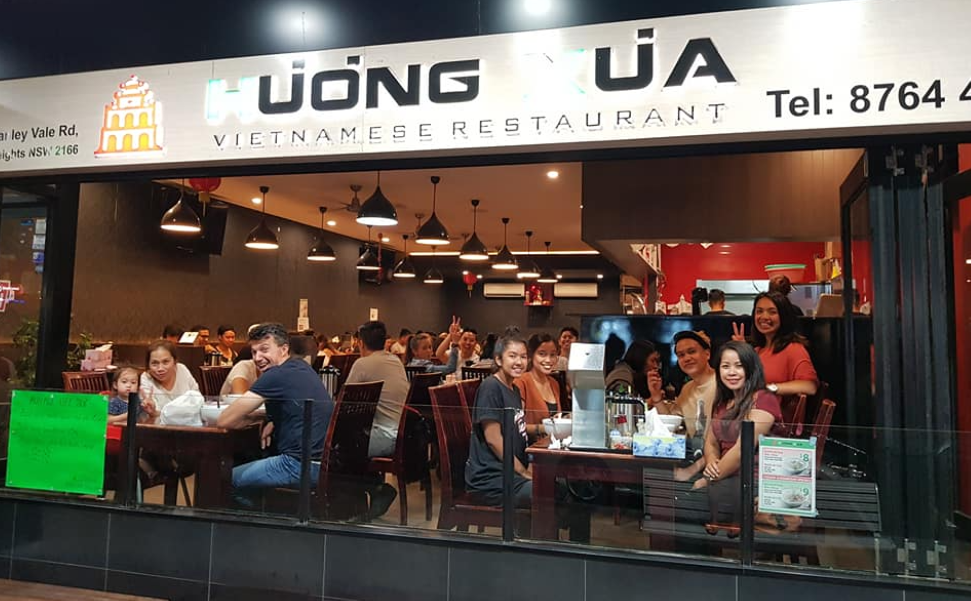 People dining inside a Vietnamese restaurant with a sign reading "Hương Xưa." The interior is warmly lit with hanging lights.