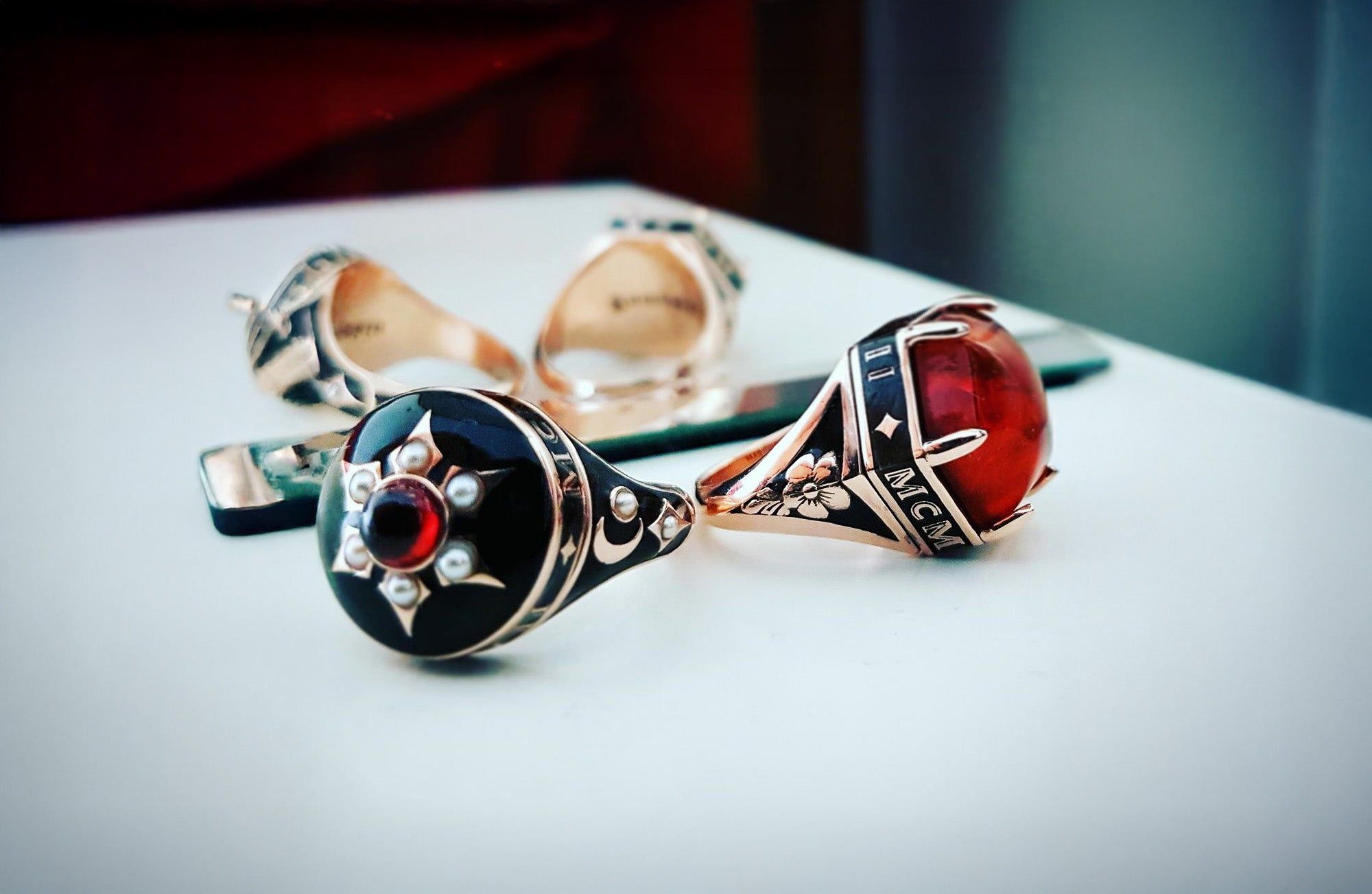 Close-up of ornate rings featuring a black and red gemstone design, placed on a reflective surface with blurred background.