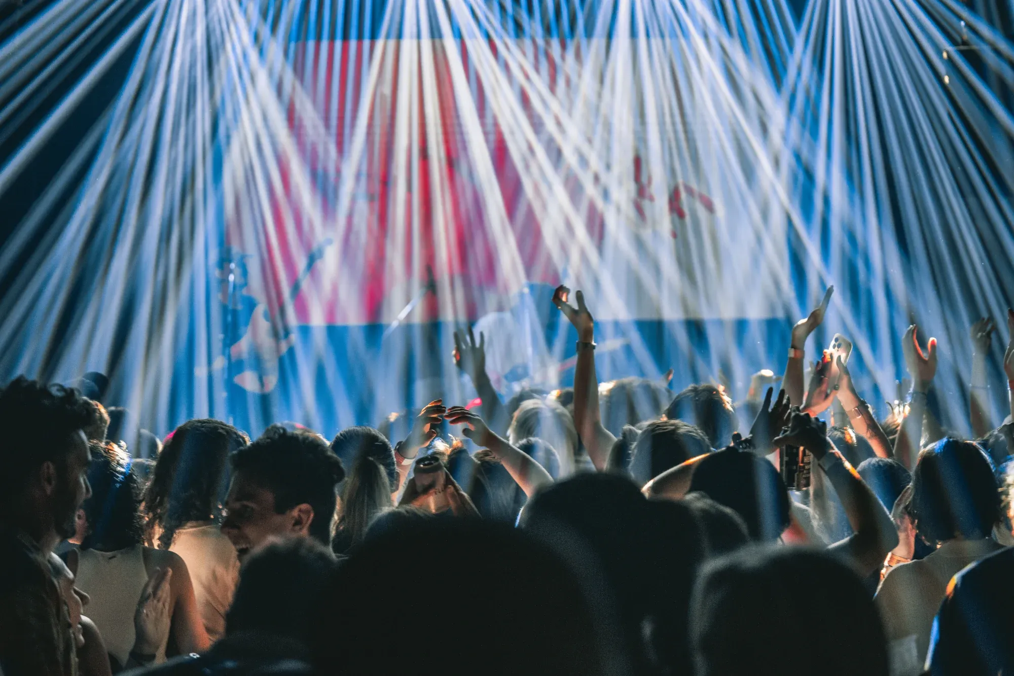 A lively concert scene with a crowd raising hands and colorful stage lights beaming down, creating an energetic atmosphere.