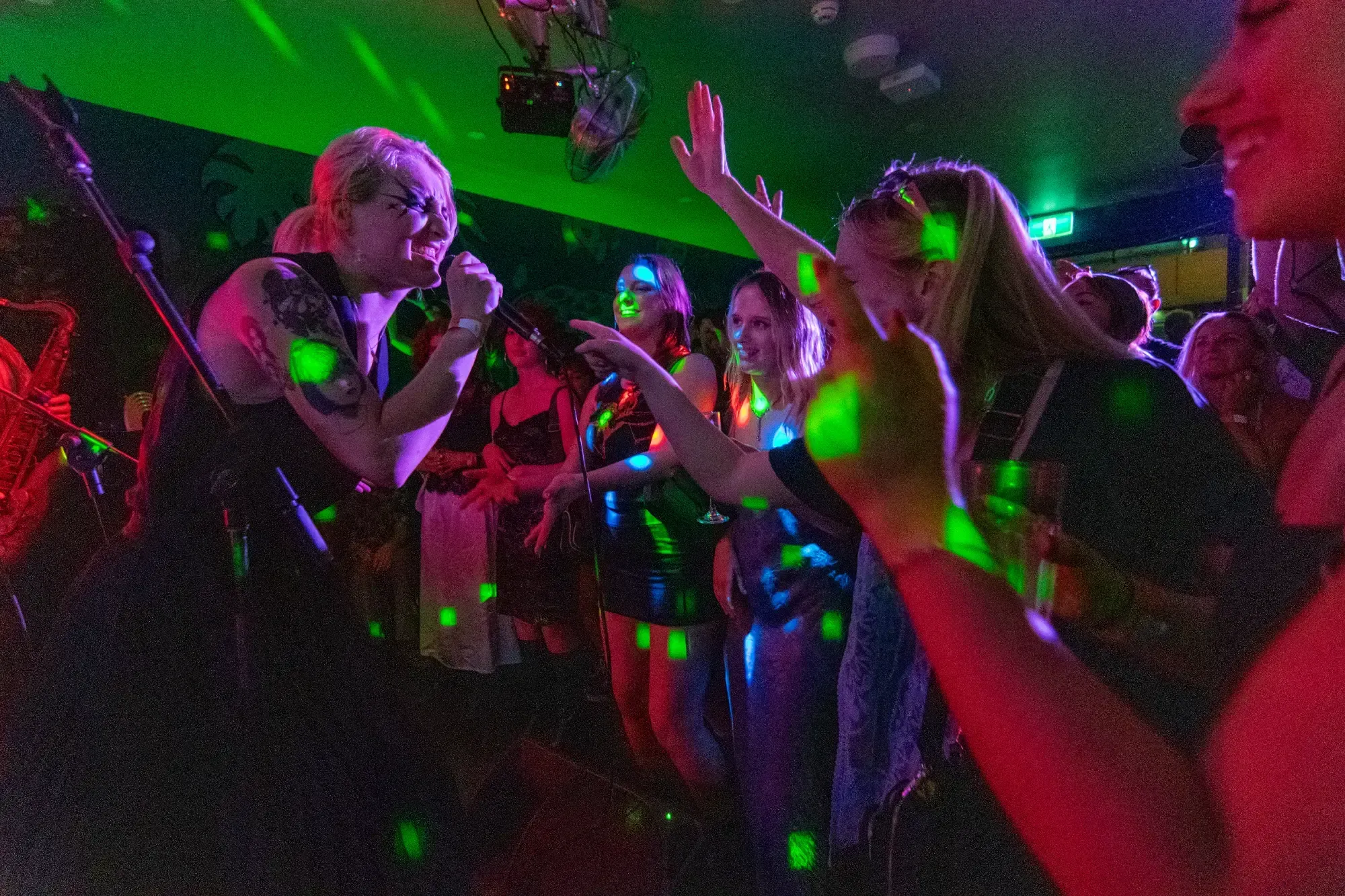 A singer performs energetically on stage, engaging with an enthusiastic crowd under colorful lights in a lively nightclub setting.