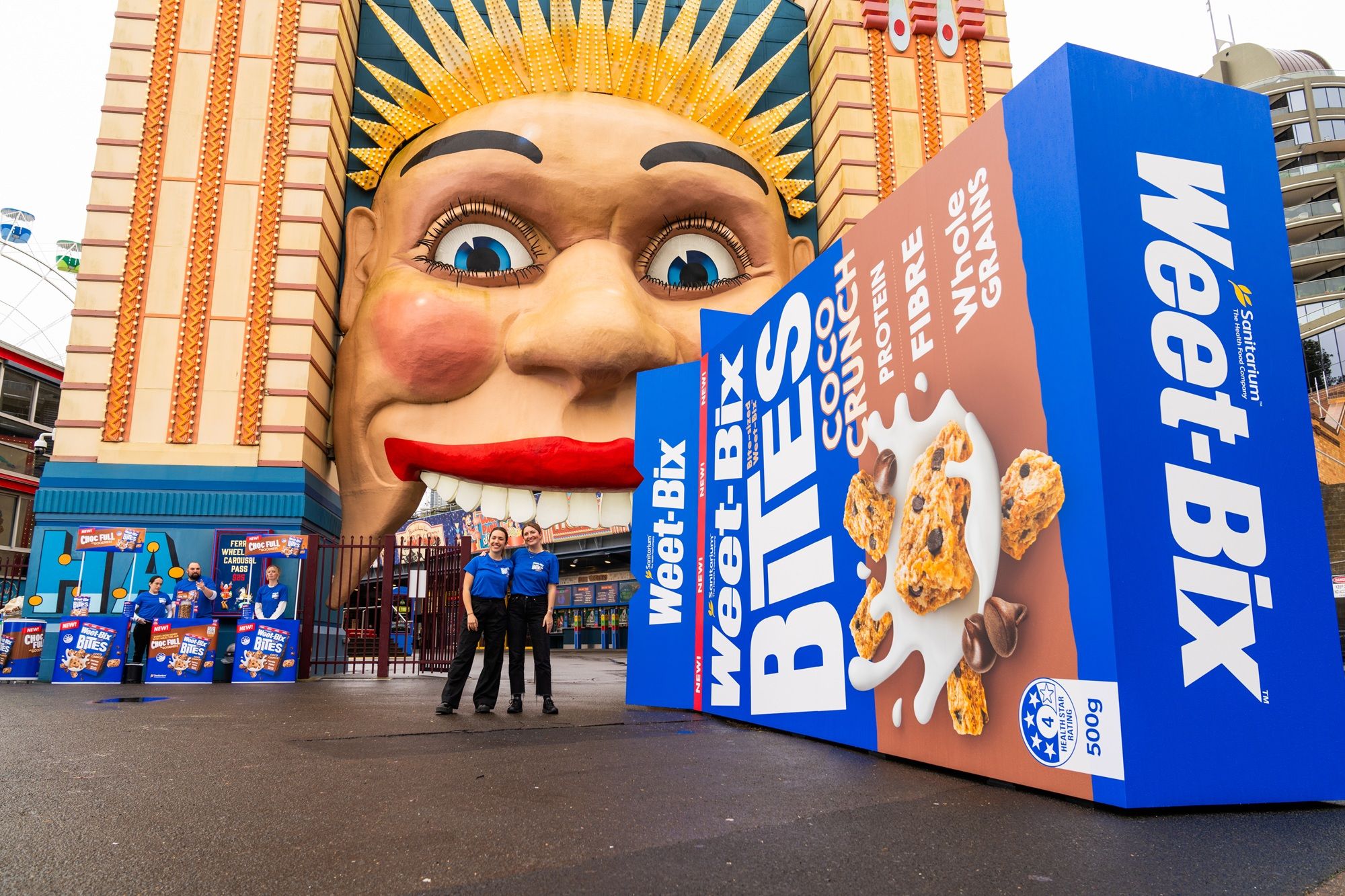 Two people standing in front of Luna Park and an oversized Weet-Bix box