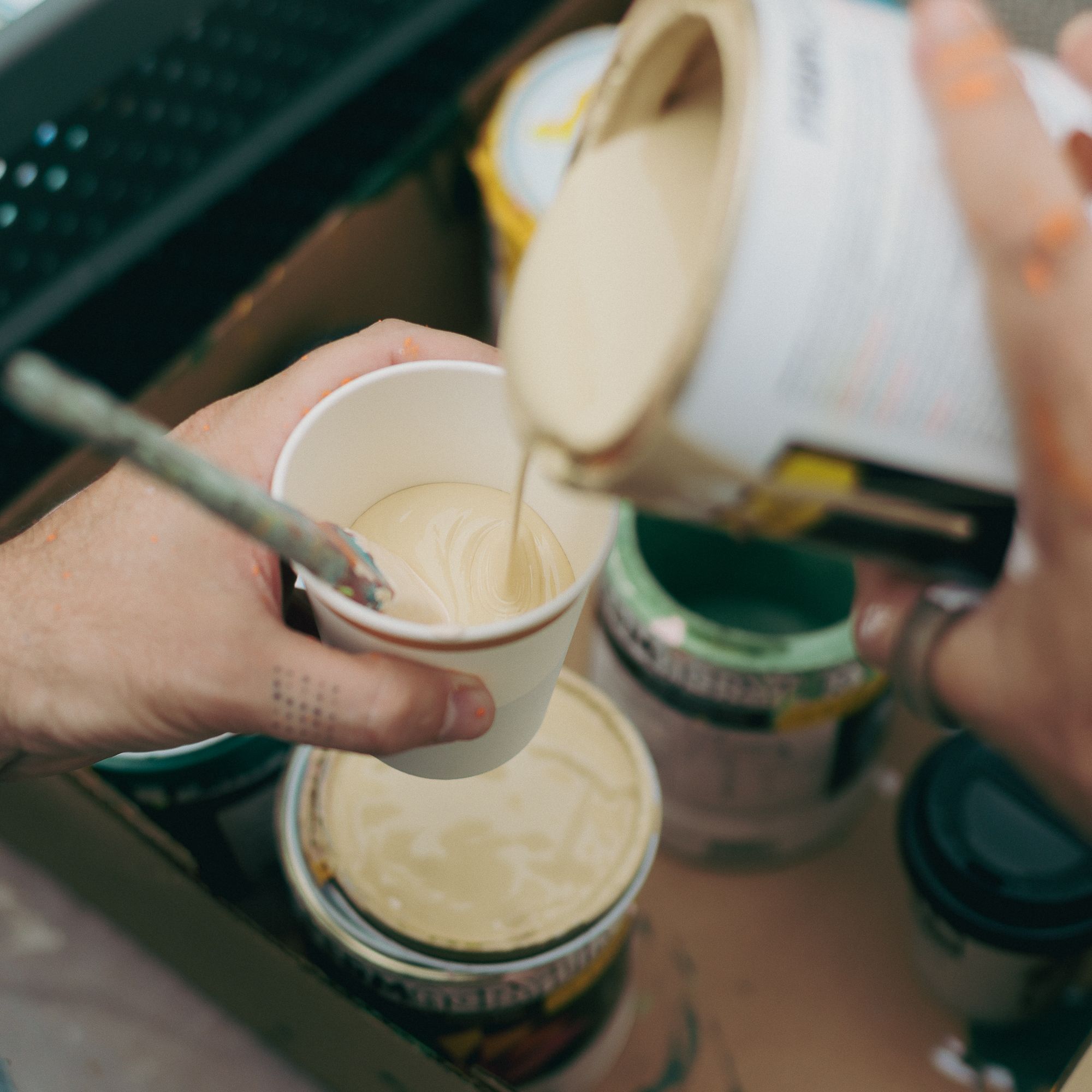 Artist hands pouring liquid paint on a cup, in a painting setting