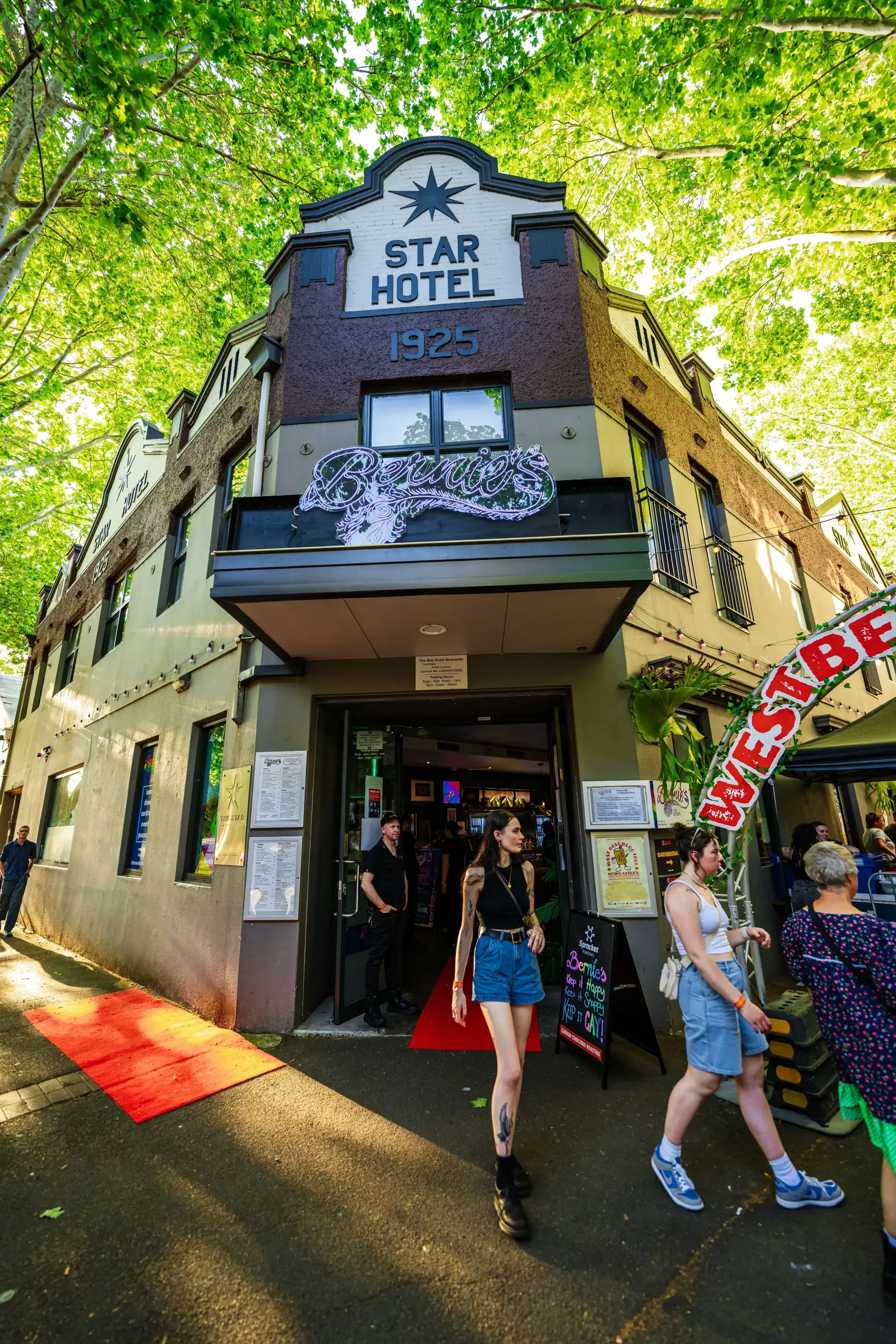 People entering and exiting the Star Hotel, built in 1925, with a "Beyoncé" sign above the entrance. Trees and a red carpet are visible.