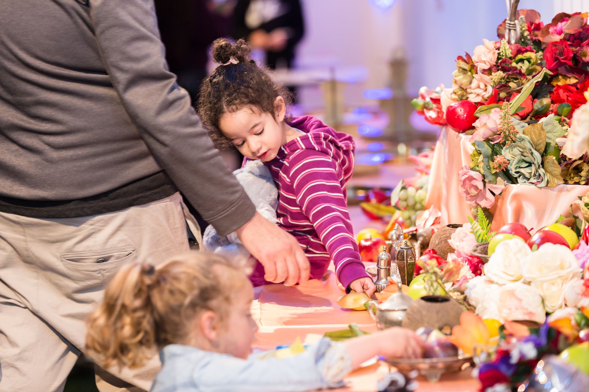 Mother and daughter placing paper food onto elaborate table decorated with fruit and flowers