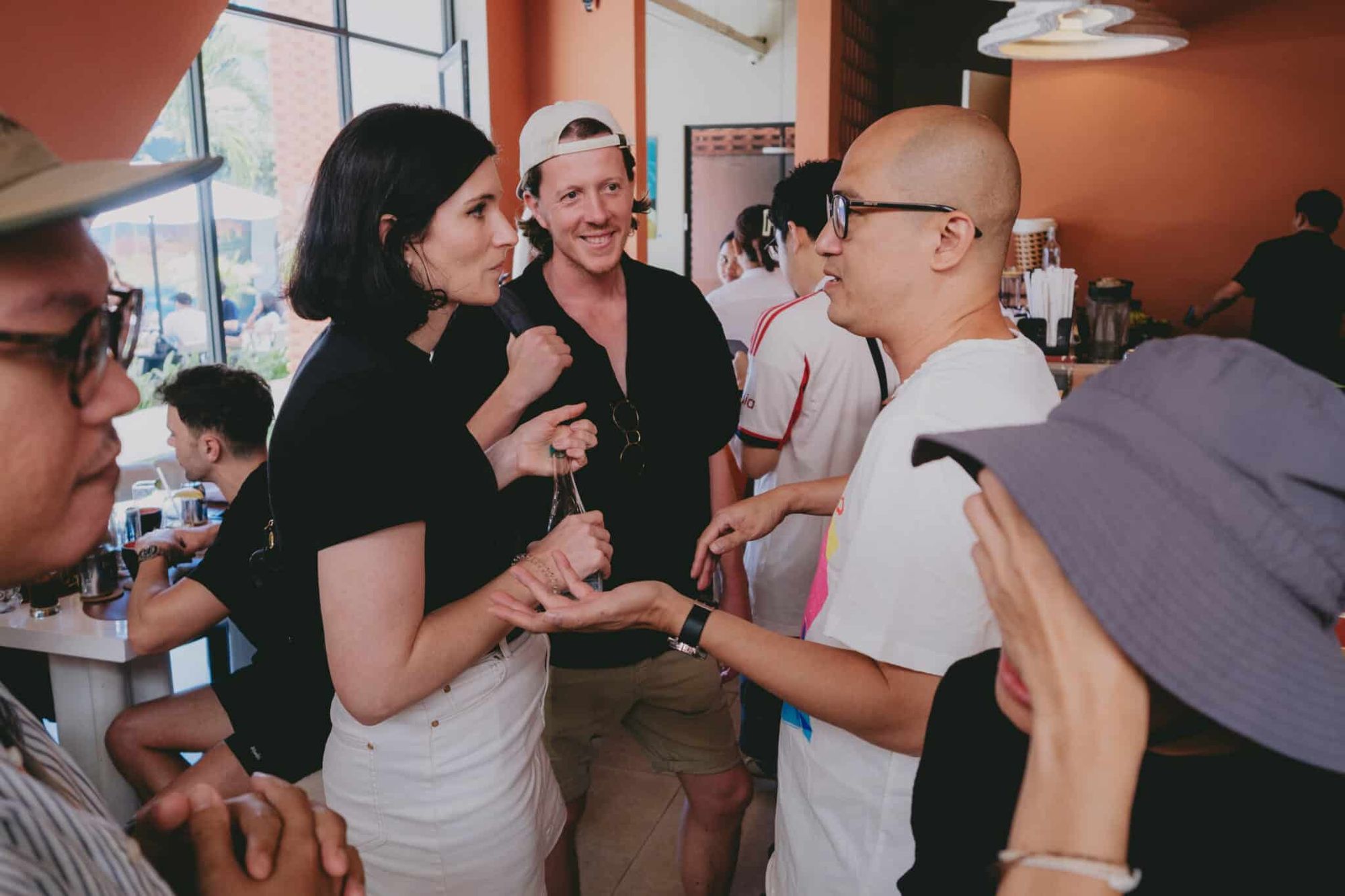 A group of people engaged in conversation inside a café, with one person gesturing while others listen attentively.