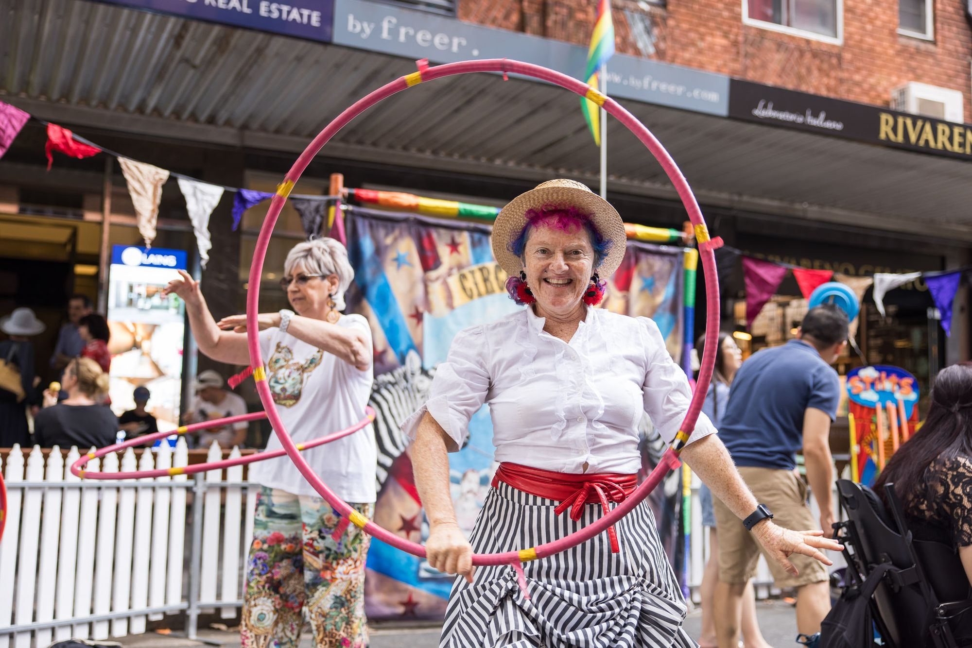 A circus performer looks through a hula hoop at the camera