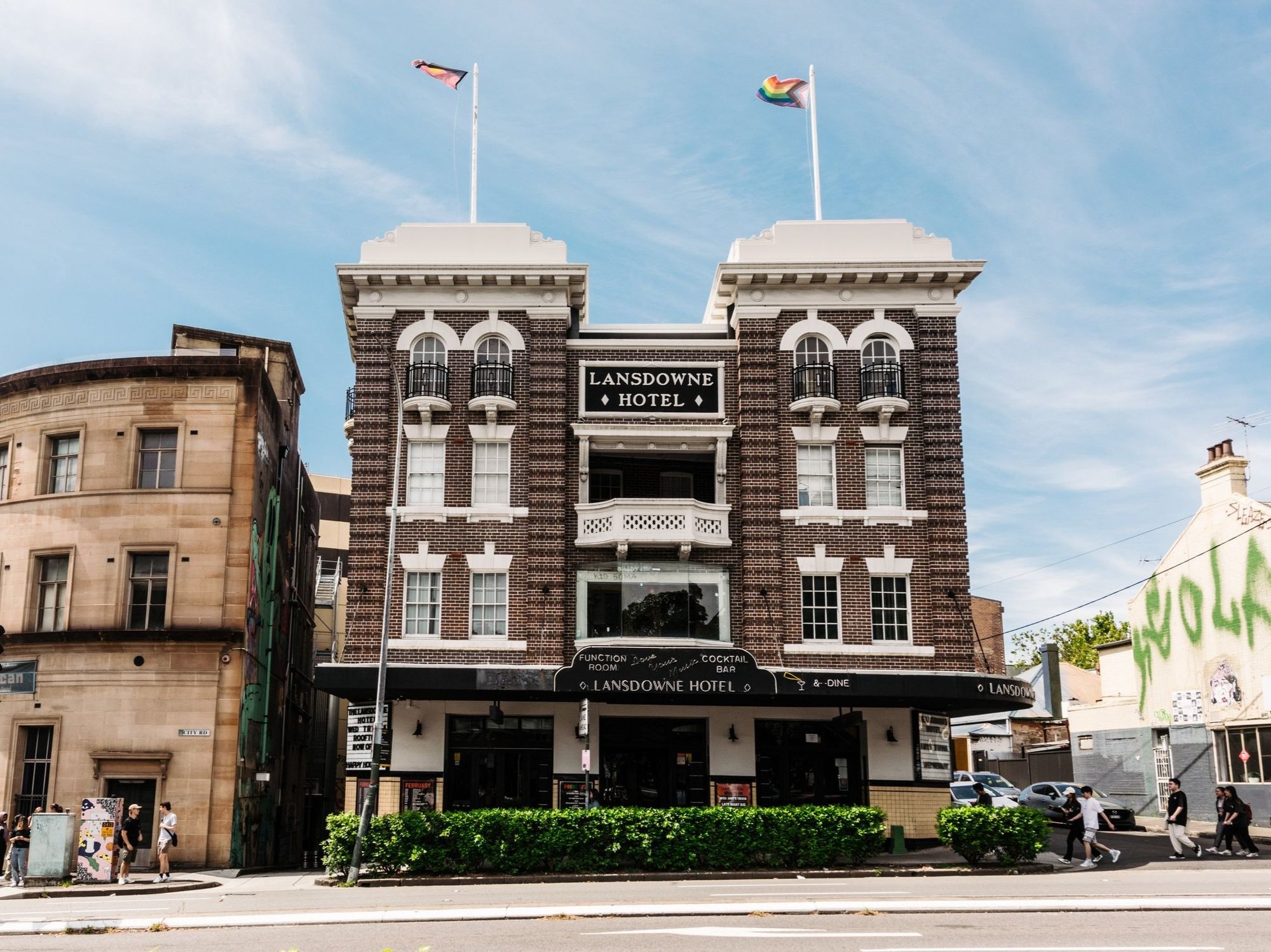 Historic Lansdowne Hotel with two flags on the roof, located on a street corner under a clear blue sky.