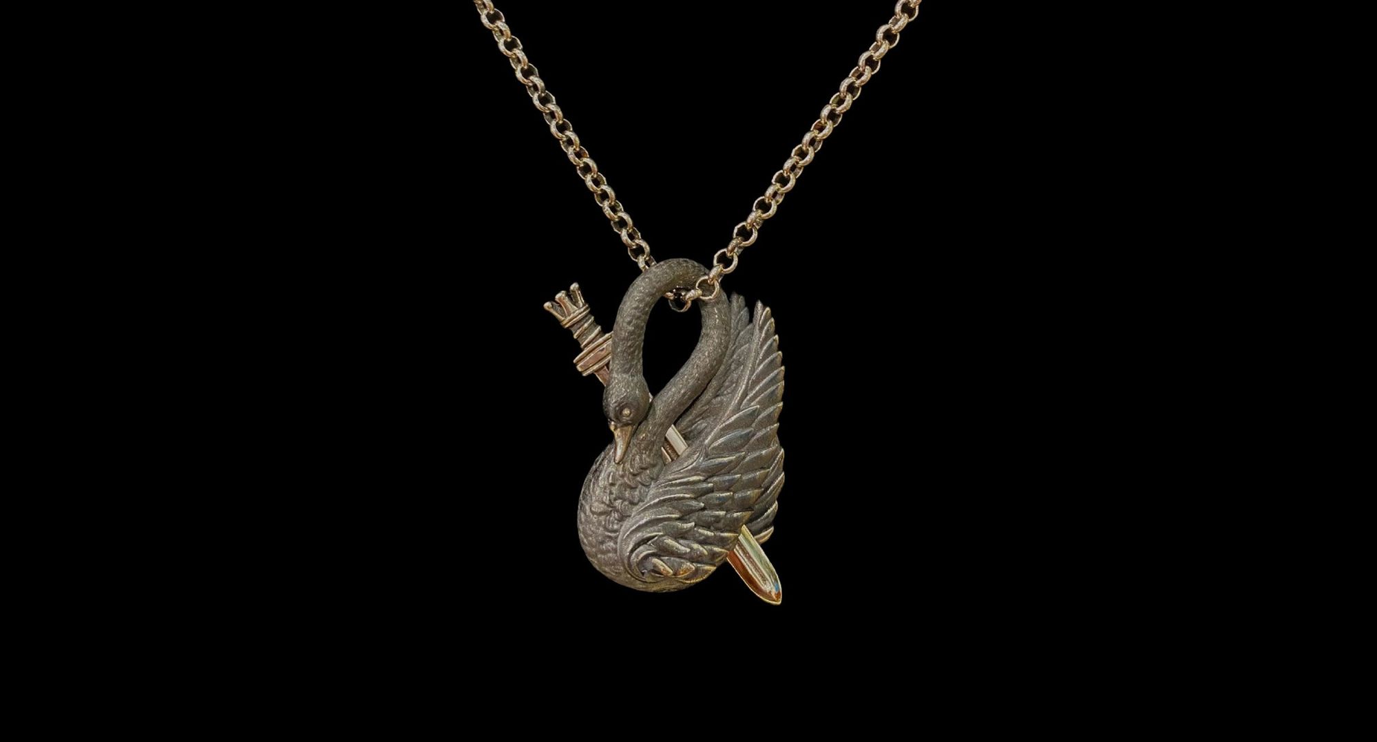 Silver swan-shaped pendant with detailed wings and a small arrow, hanging on a chain against a black background.