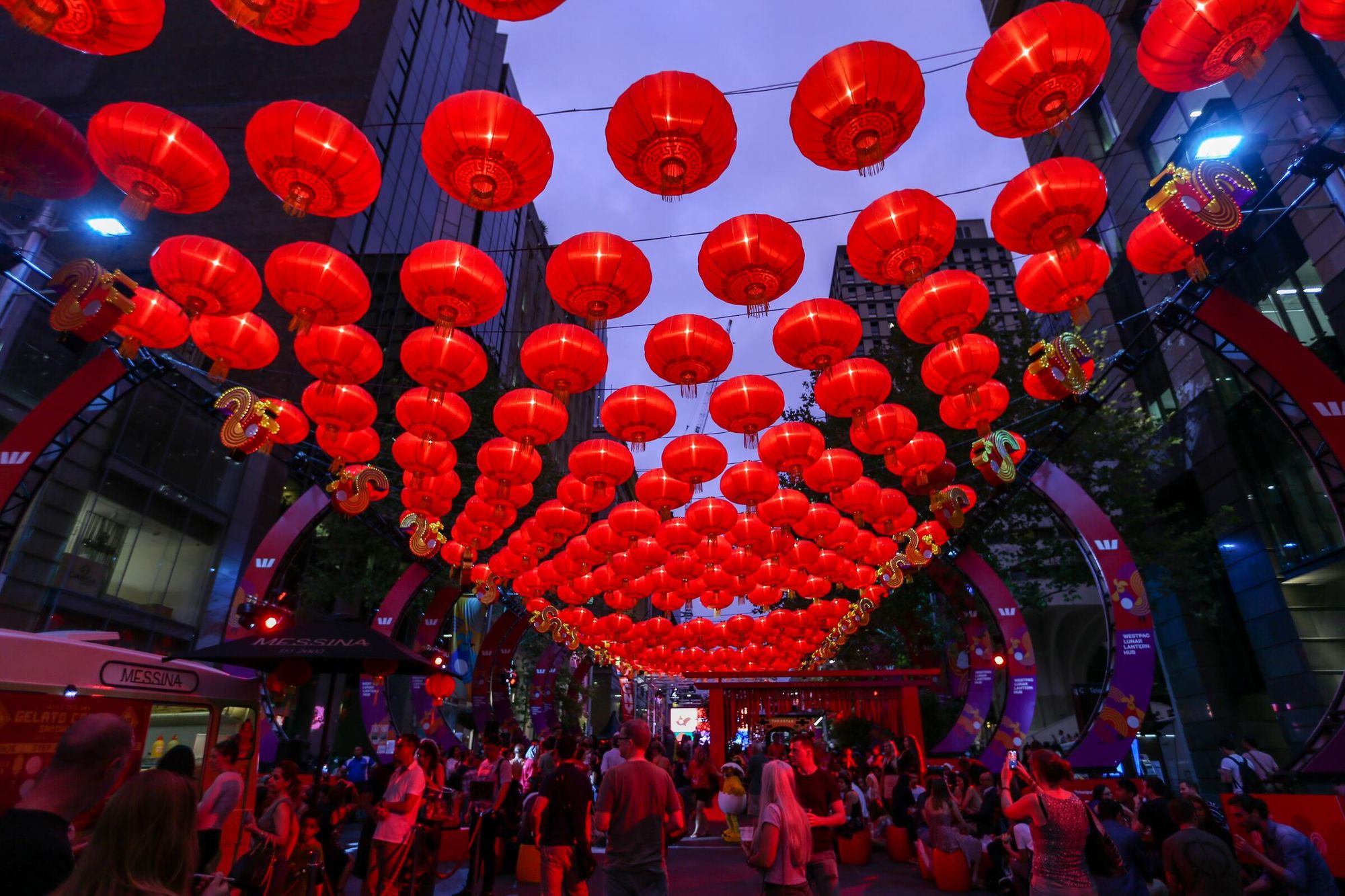 Rows of brightly lit red lanterns stretch over a lively evening street with lots of people