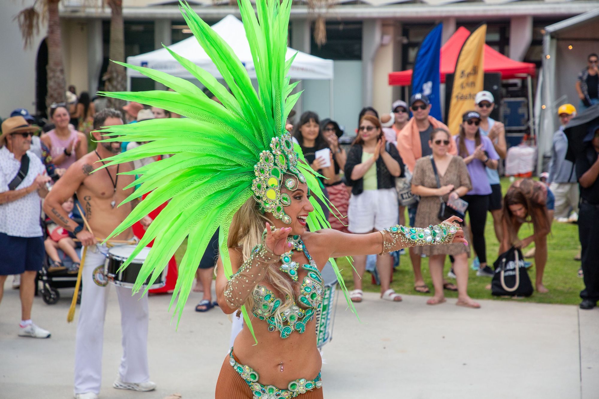 A dancer in a vibrant green feathered costume performs in front of a crowd at an outdoor event.