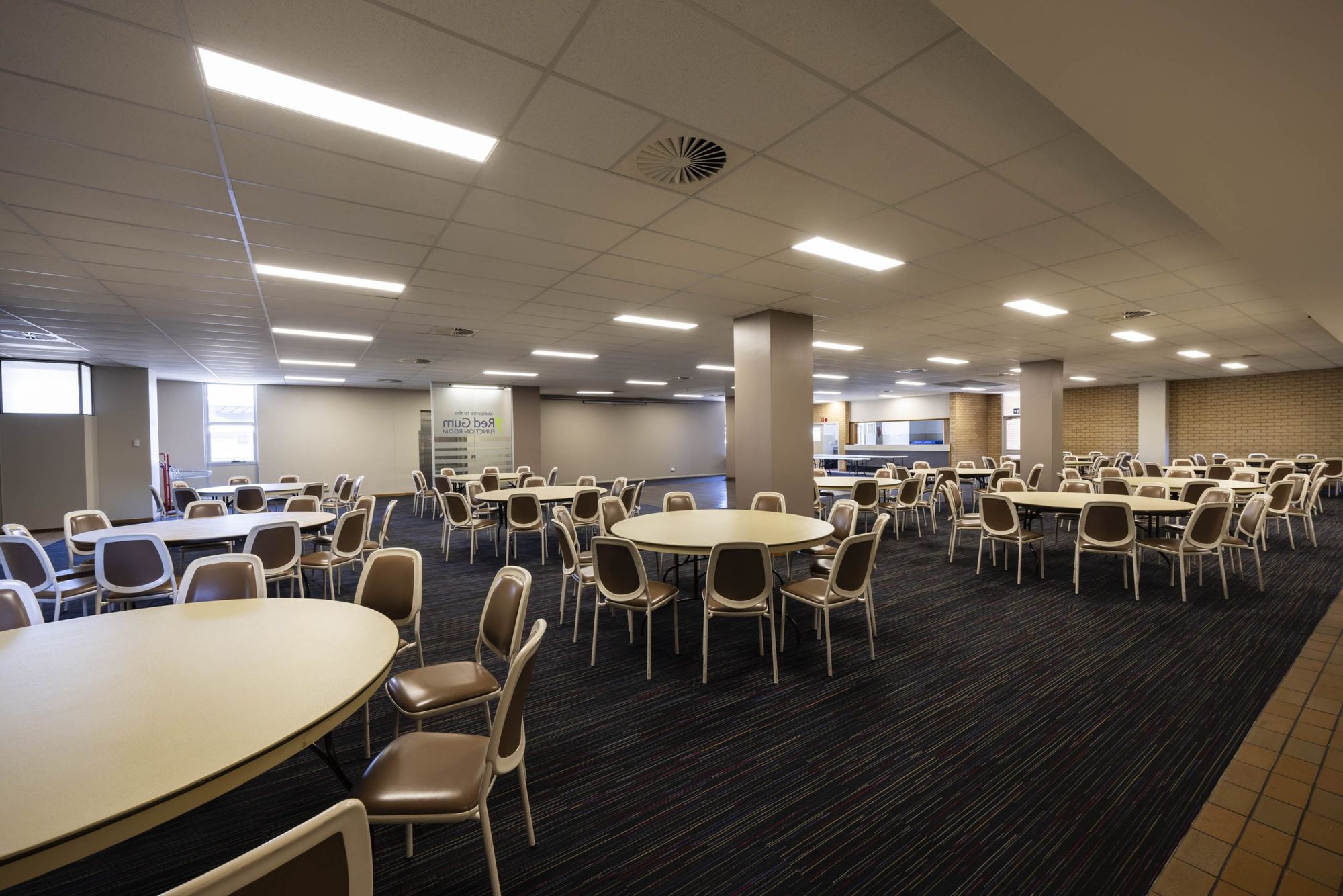 Spacious conference room with round tables, brown chairs, and bright overhead lighting.