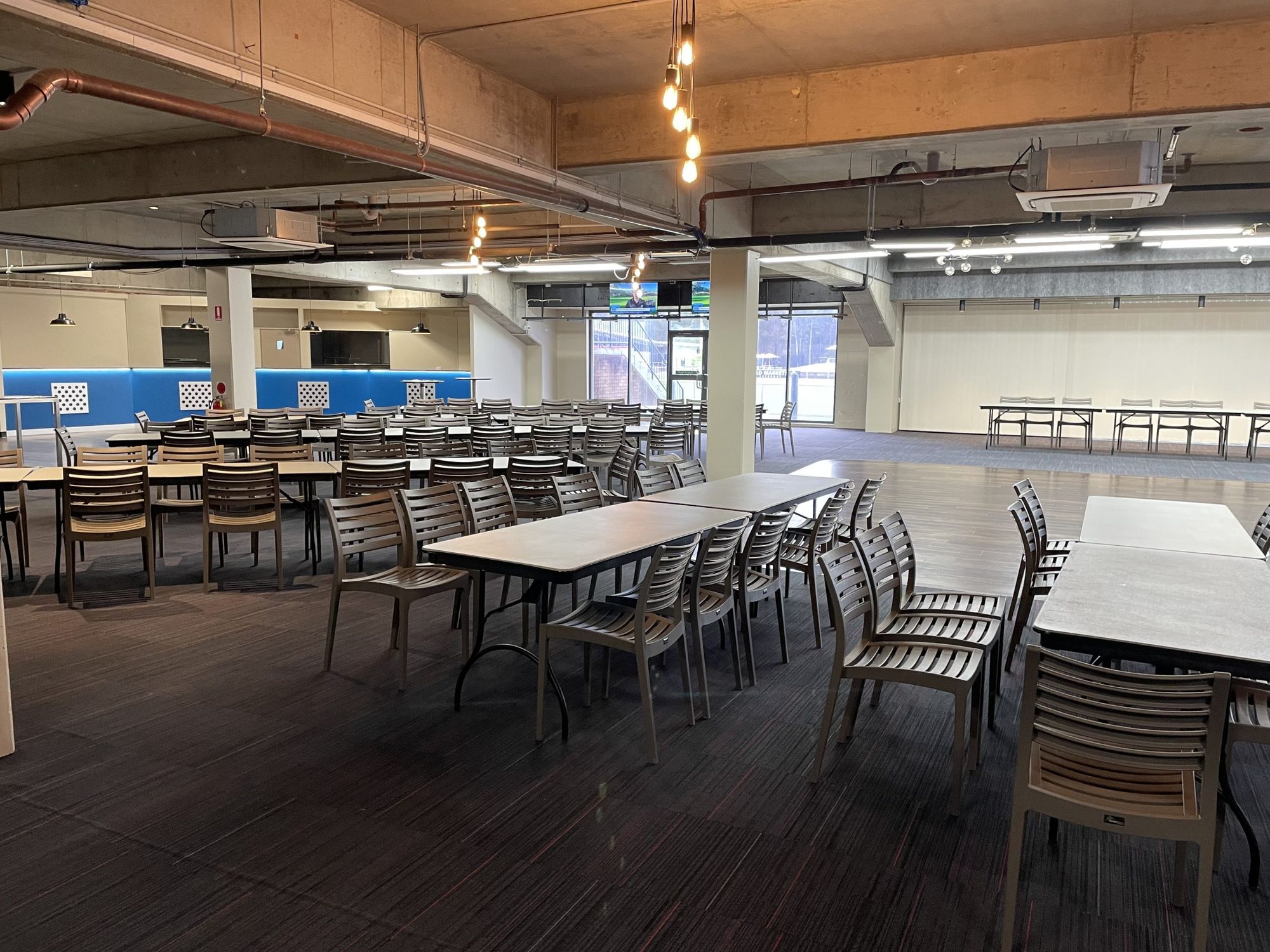 Spacious conference room with round tables, brown chairs, and bright overhead lighting.