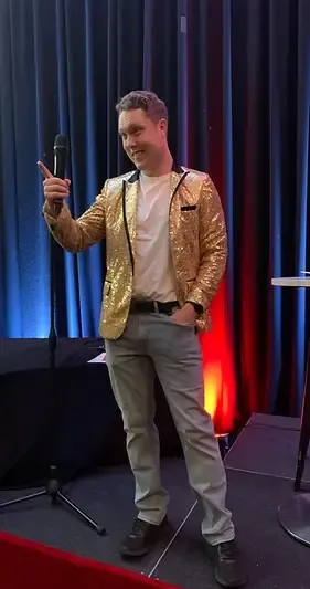 Trivia host in gold jacket presenting with a microphone on stage at an indoor event