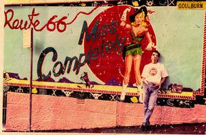 Person in sunglasses and jeans leans against a wall with Route 66 mural featuring "Miss Completely" and a cowgirl illustration.
