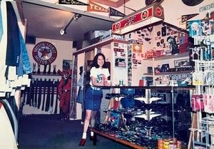 A person in a casual outfit stands inside a souvenir shop featuring Texas-themed signs, magnets, and memorabilia.