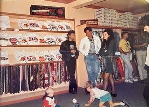 Store interior with people browsing sports merchandise; two toddlers play on the floor. Shelves display T-shirts and sports apparel.