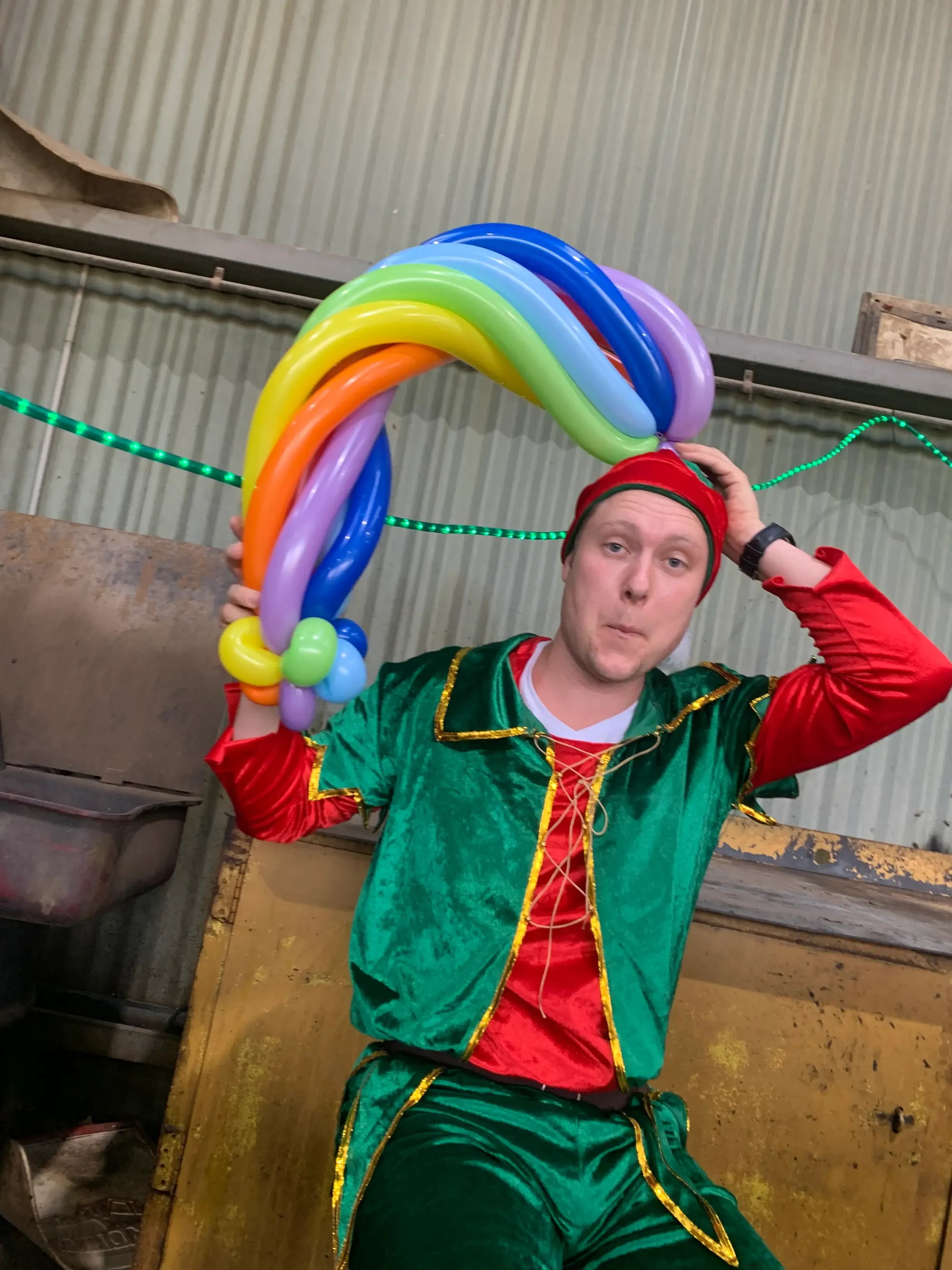 Balloon twister dressed as a Christmas elf holding a colourful balloon creation