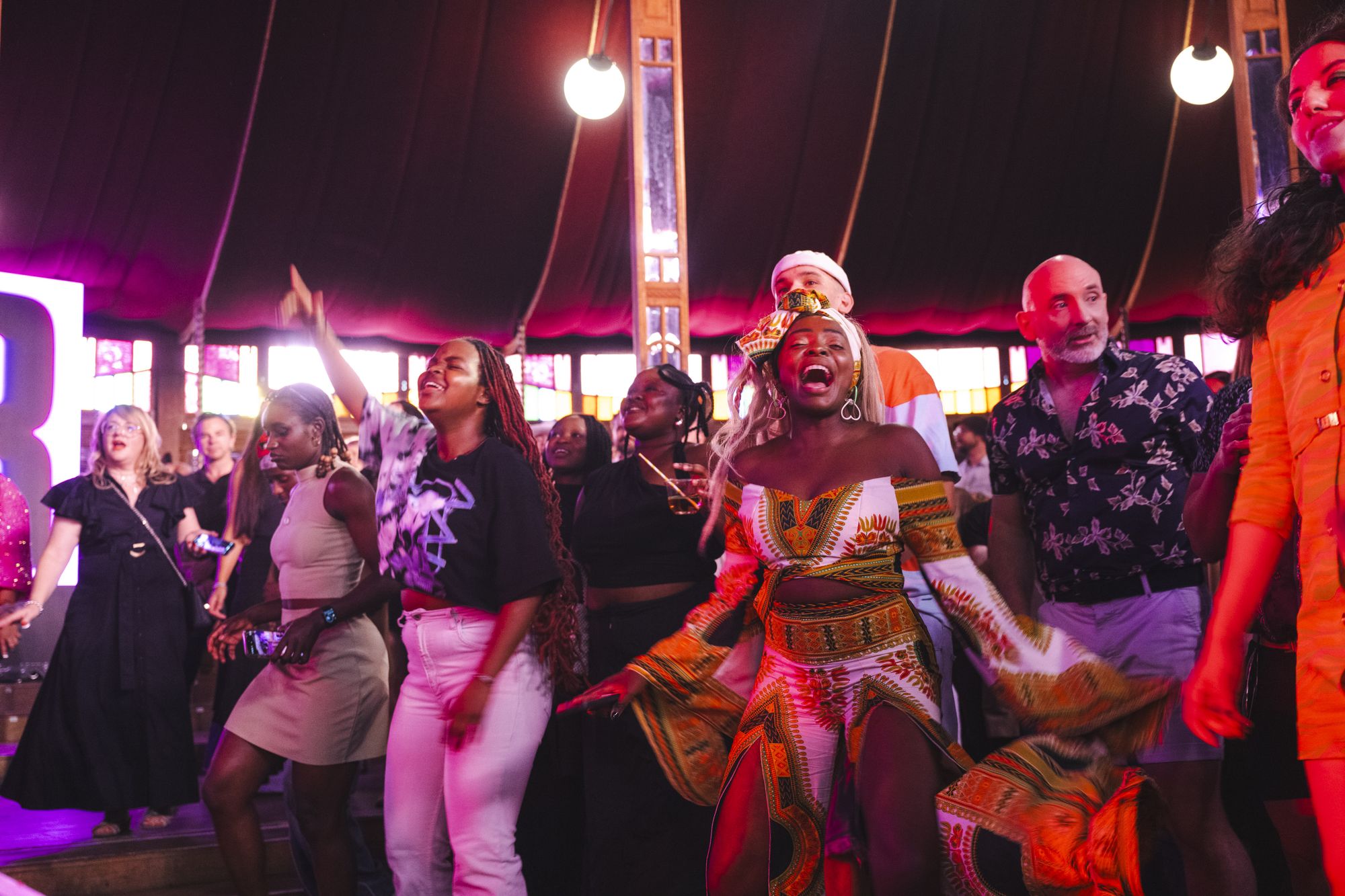 A group of people joyfully sing inside the Sydney Spiegeltent while watching the Soweto Gospel Choir perform