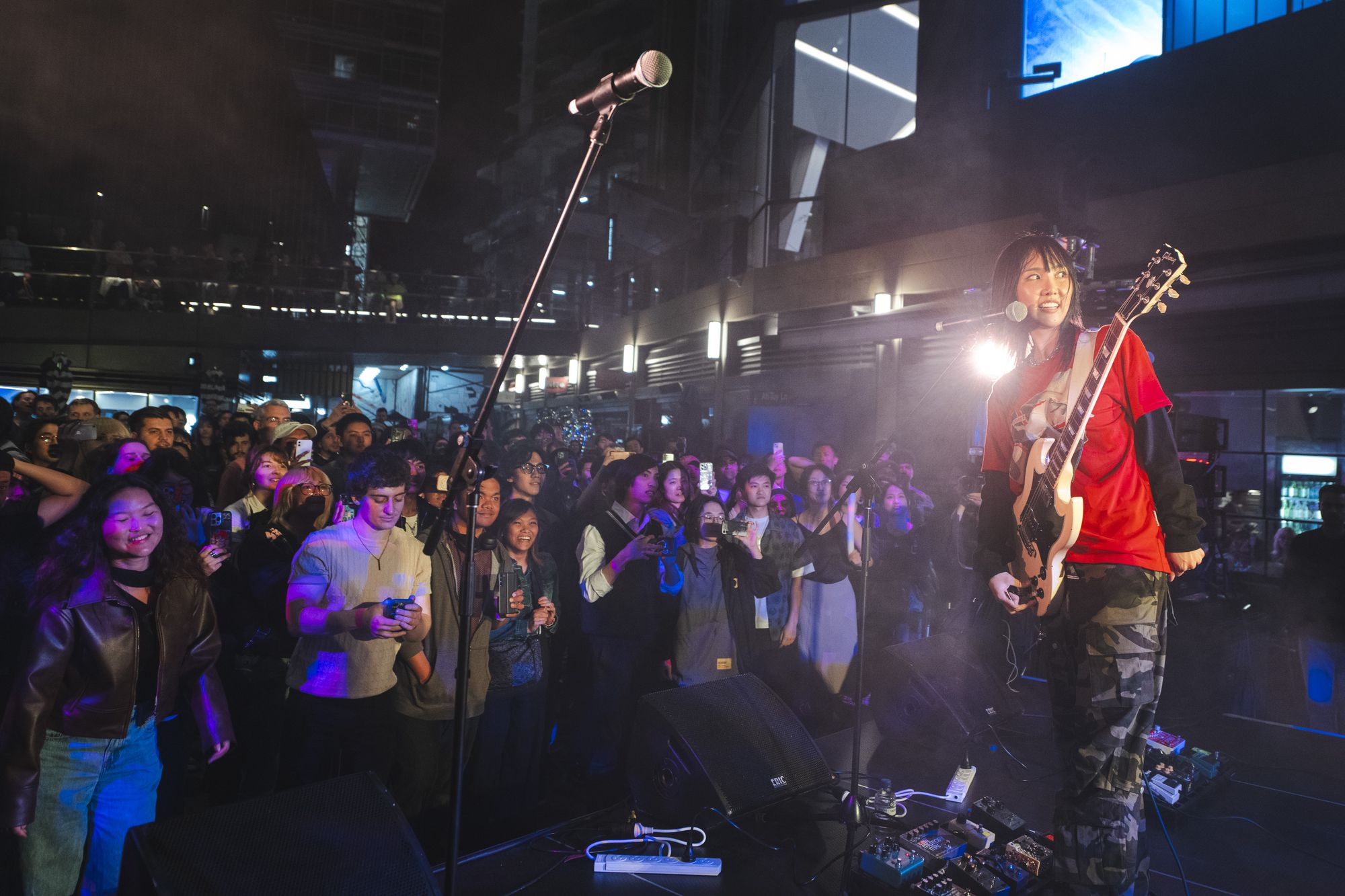 MEMI, a South Korean guitarist, stands on stage in front of a cheering crowd at Sydney Place