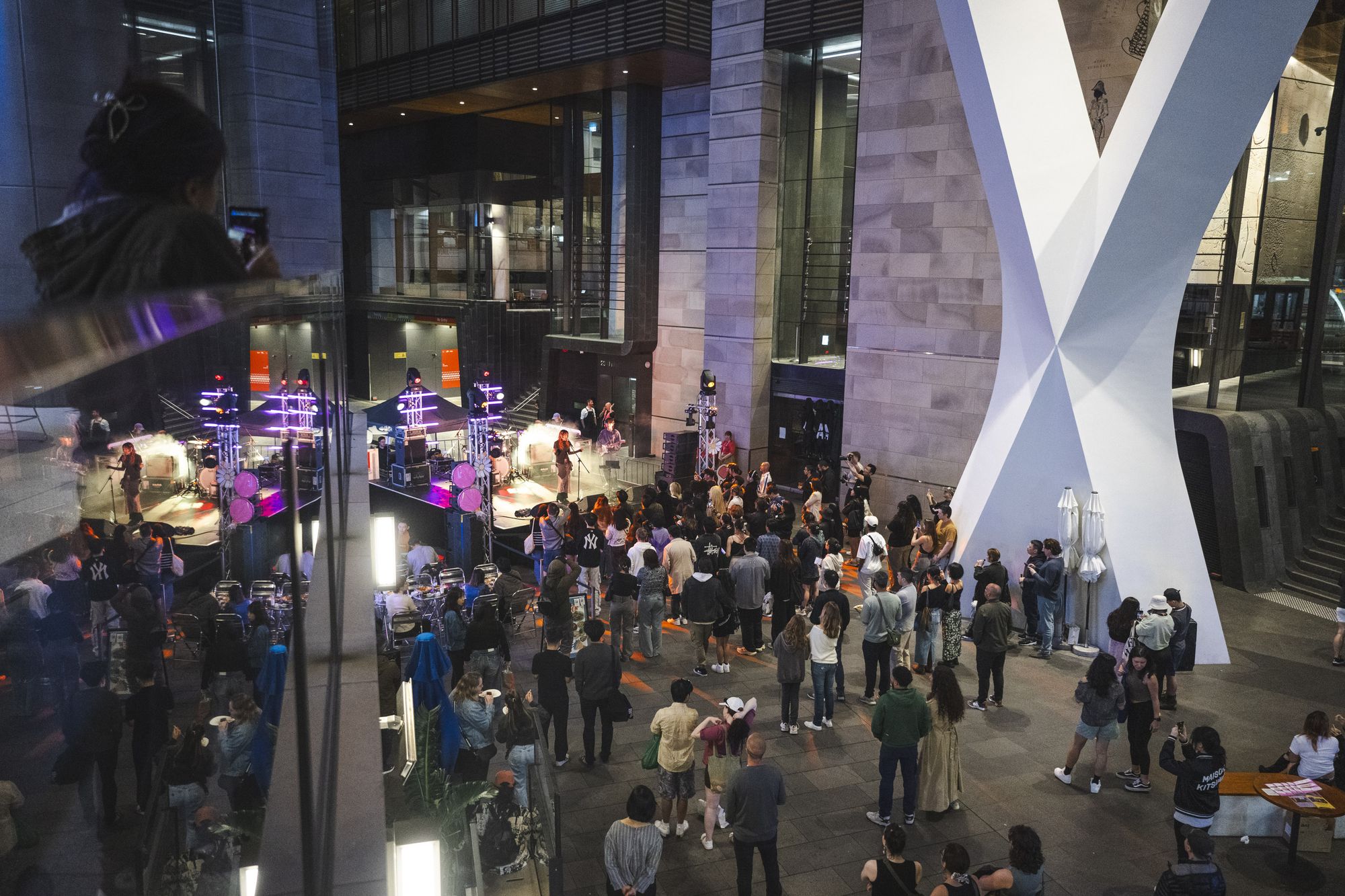A lively crowd gathers around a brightly lit stage in Sydney Place, the entry to a building